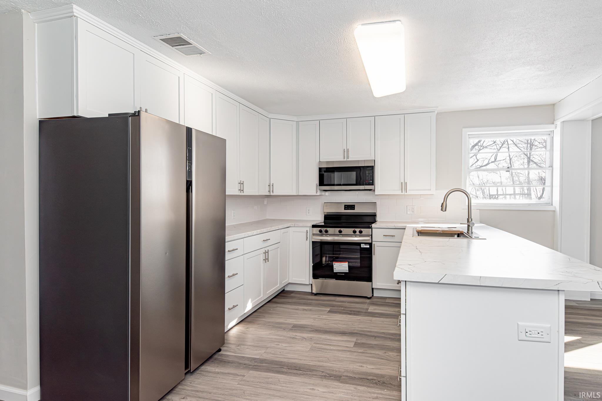 Kitchen with stainless steel appliances, a peninsula, white cabinets, a textured ceiling, and light wood-style flooring