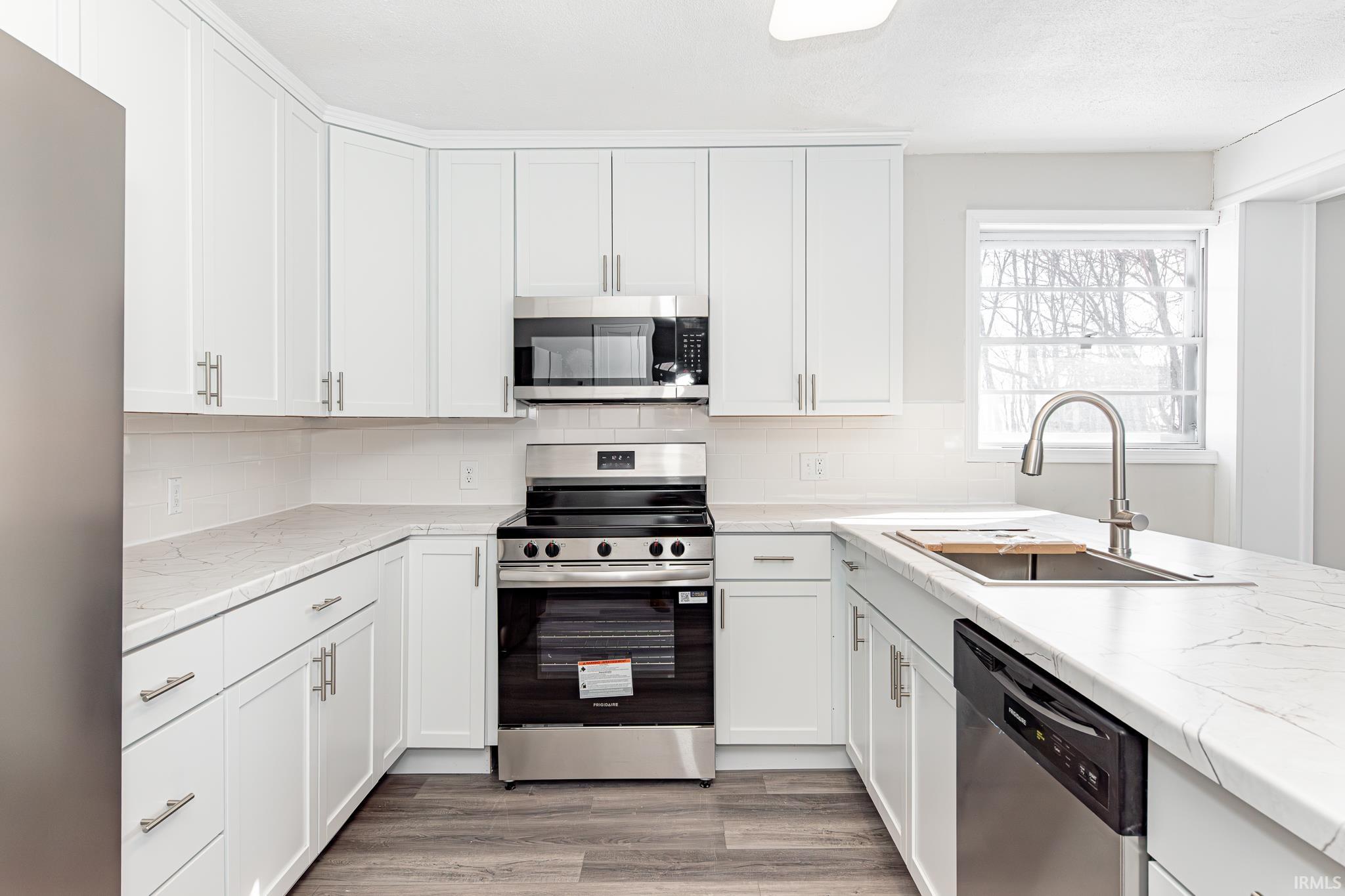 Kitchen featuring stainless steel appliances, tasteful backsplash, white cabinetry, and light wood-style flooring