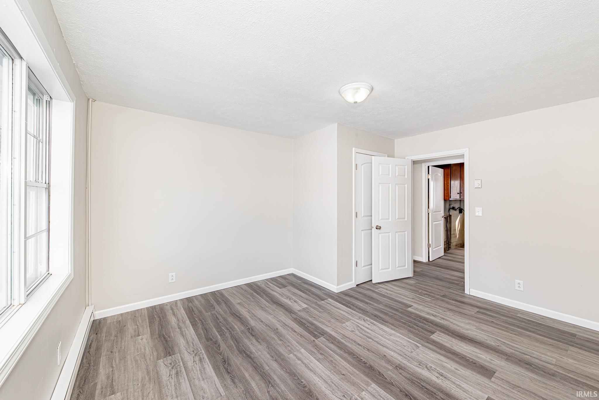 Empty room with baseboard heating, wood finished floors, and a textured ceiling
