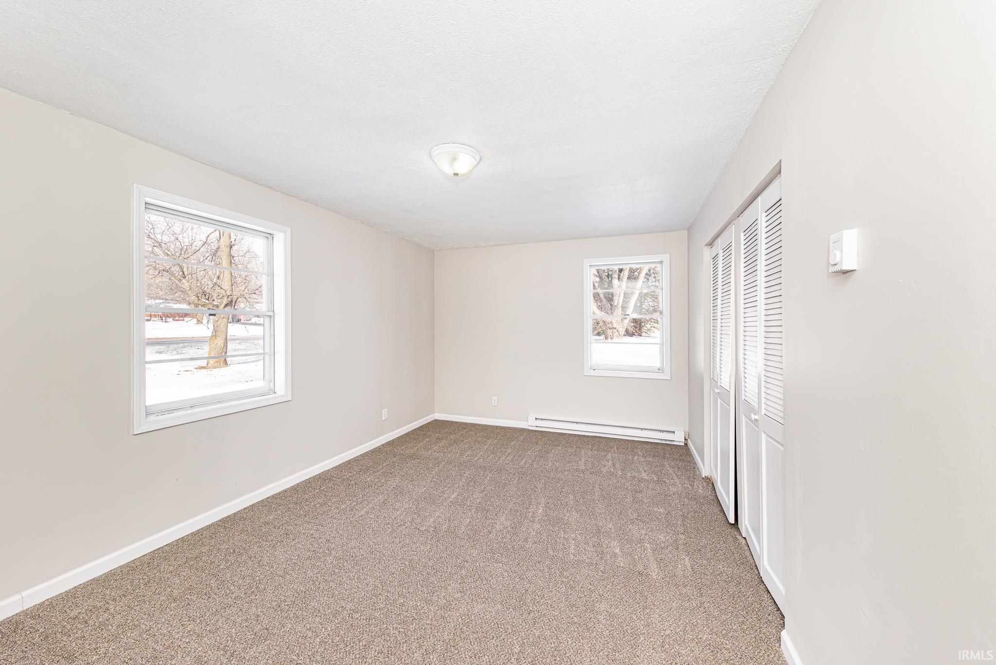 Unfurnished bedroom with light carpet, a closet, and a baseboard heating unit