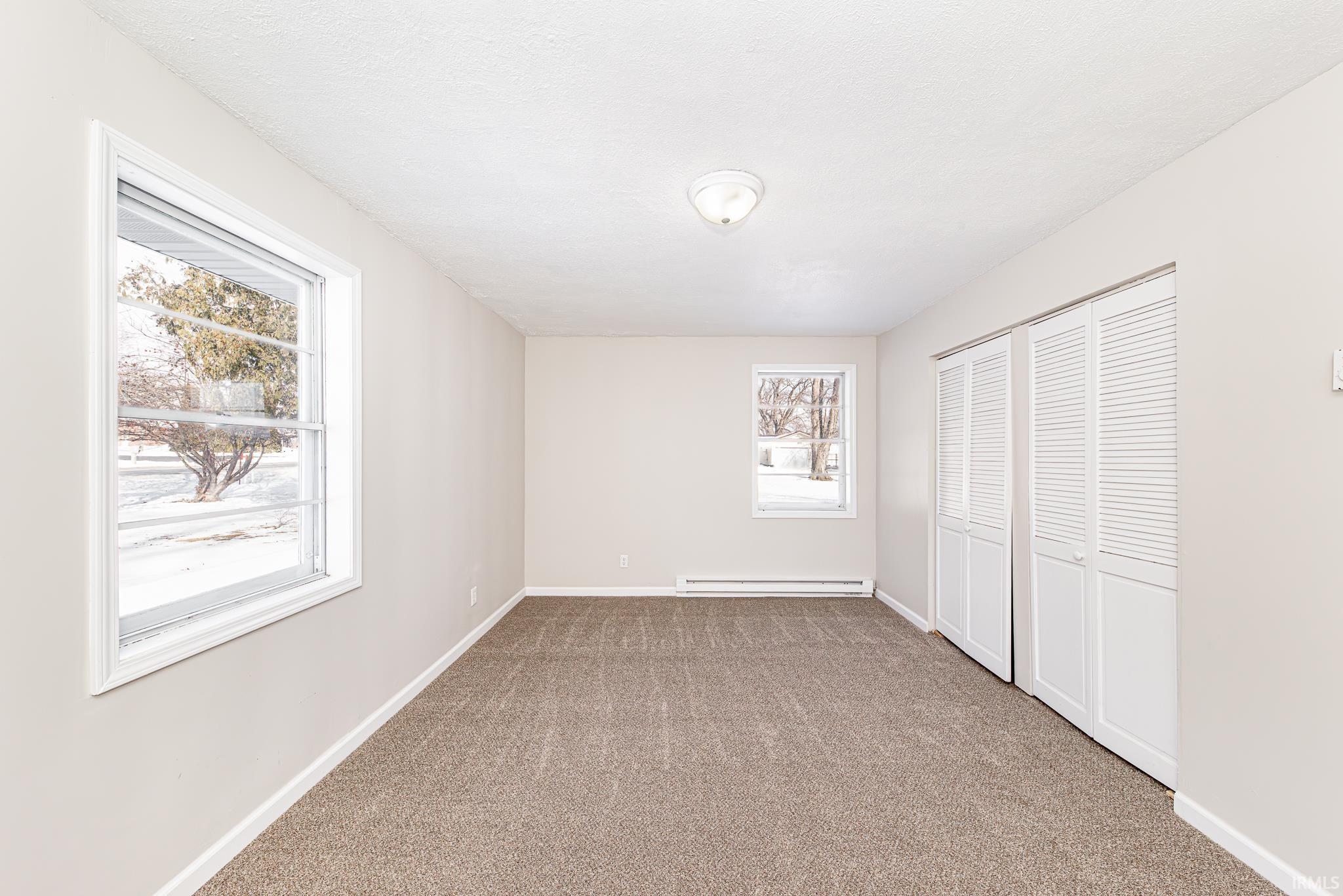 Unfurnished bedroom with a closet, carpet flooring, and baseboard heating