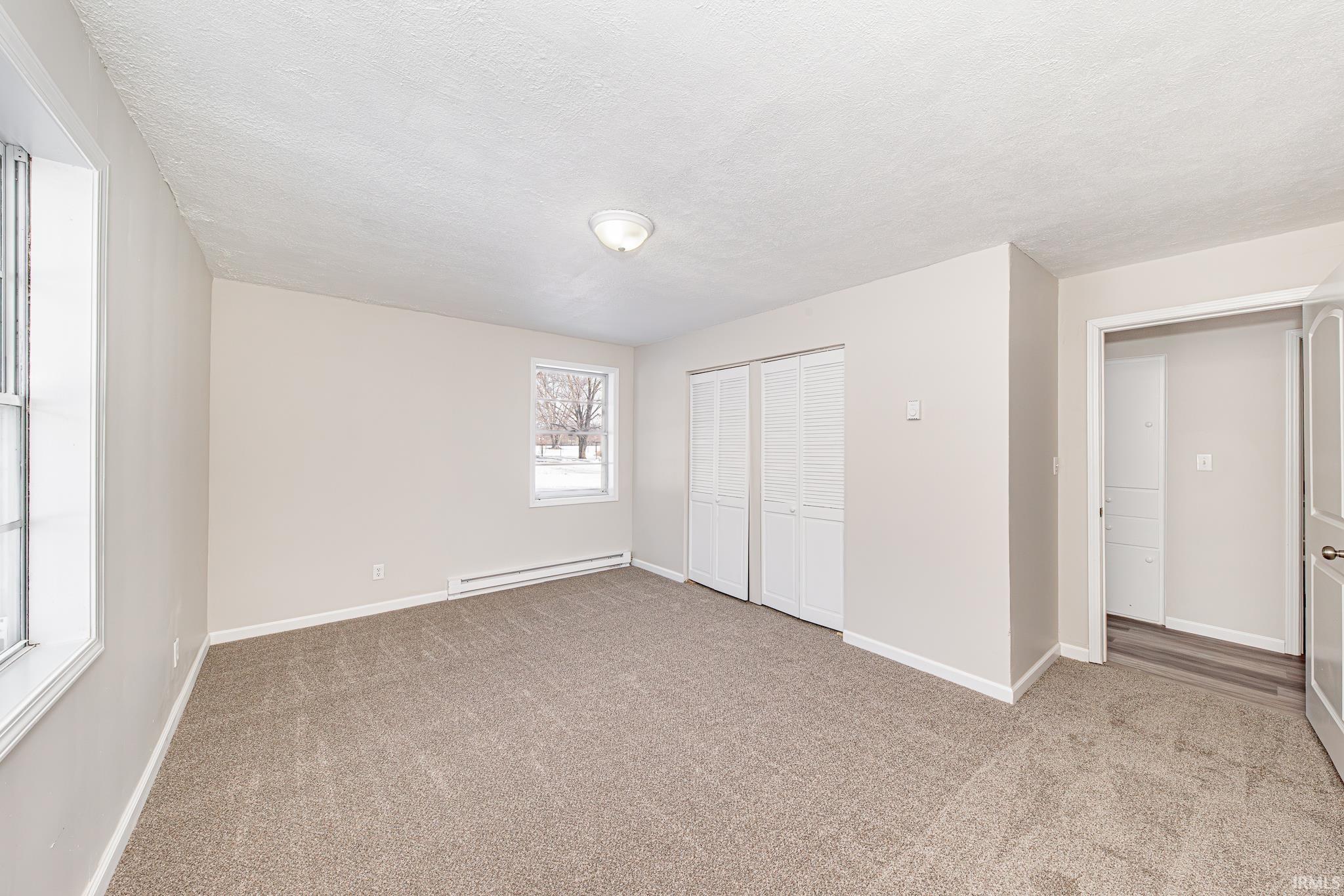 Unfurnished bedroom with a baseboard heating unit, light carpet, a closet, and a textured ceiling