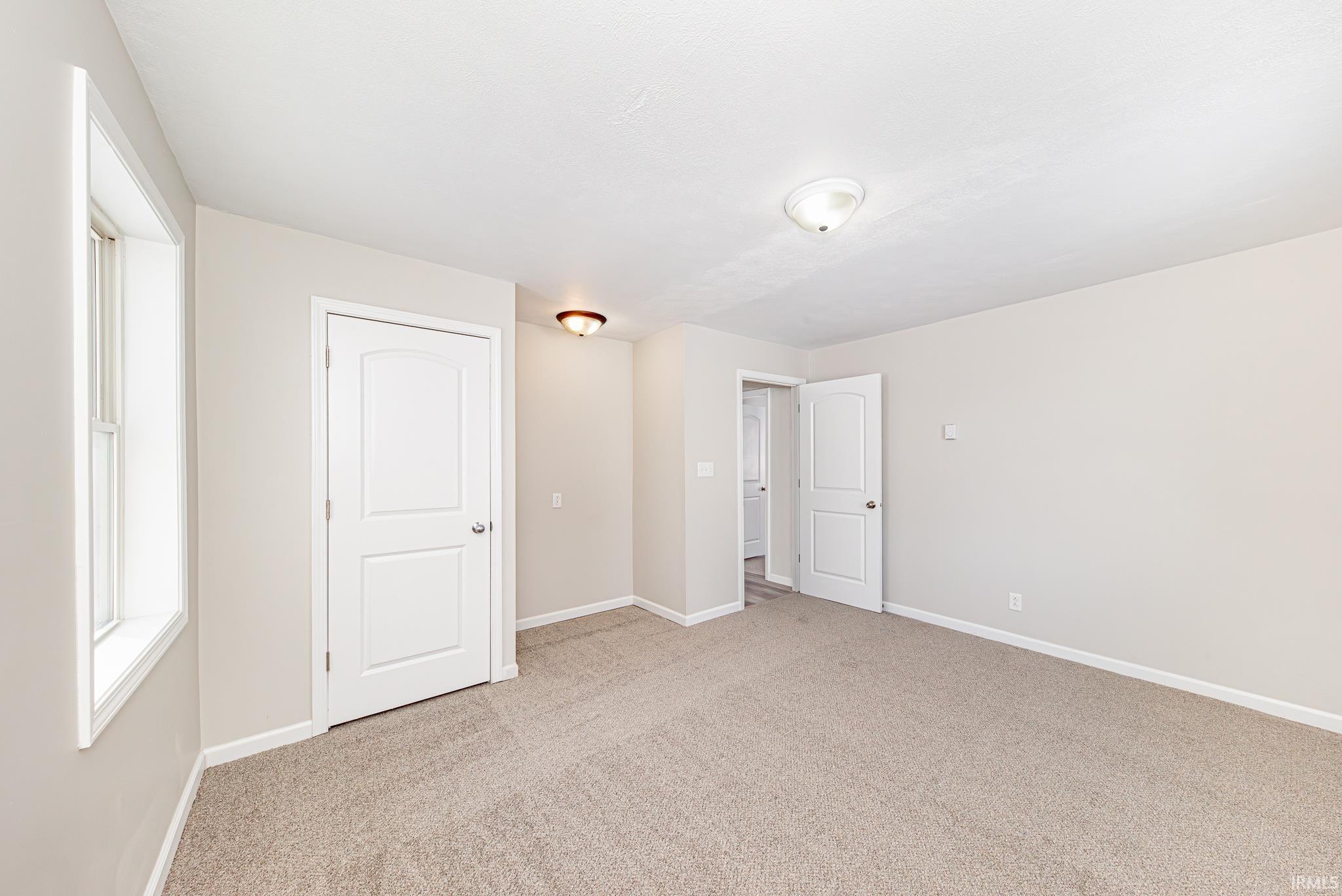 Unfurnished bedroom with baseboards and light colored carpet
