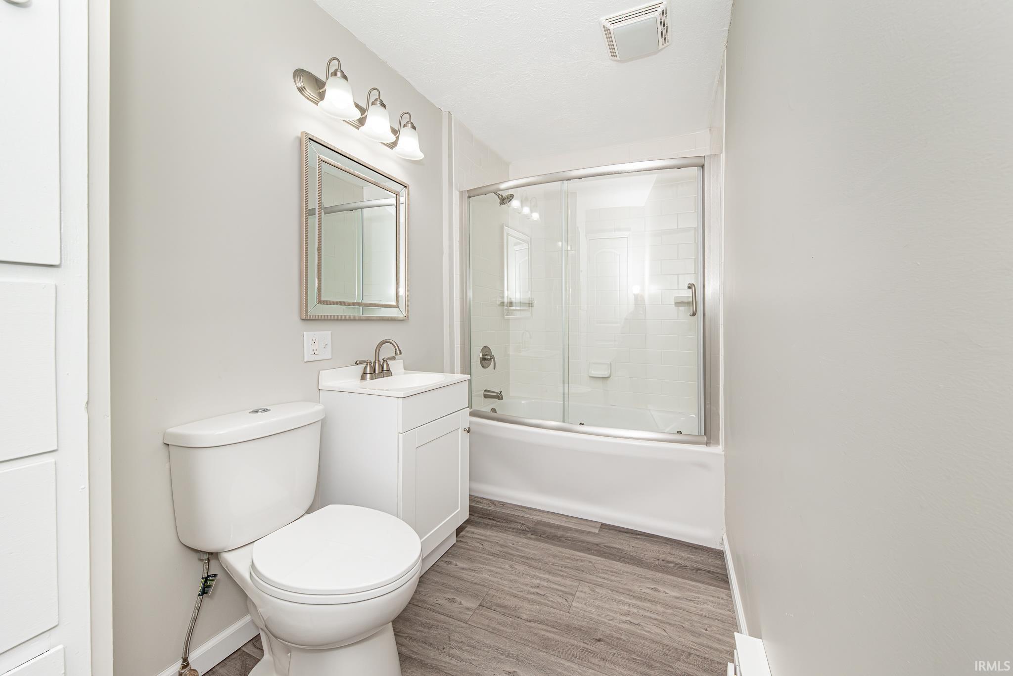 Full bath with combined bath / shower with glass door, vanity, and light wood finished floors