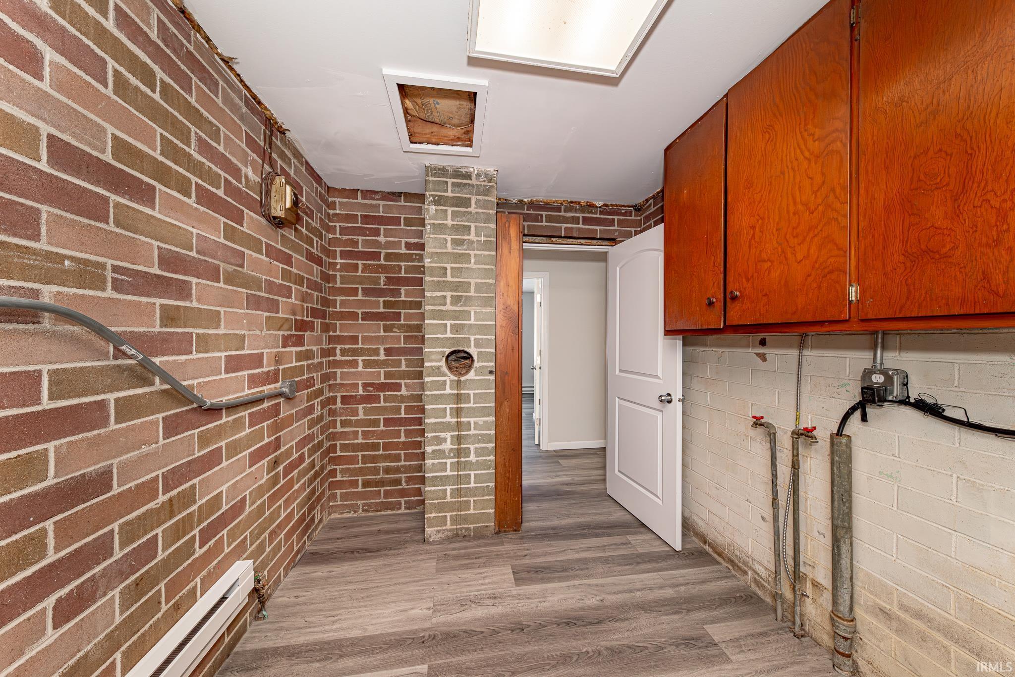 Laundry area with baseboard heating, cabinet space, brick wall, washer hookup, and light wood finished floors
