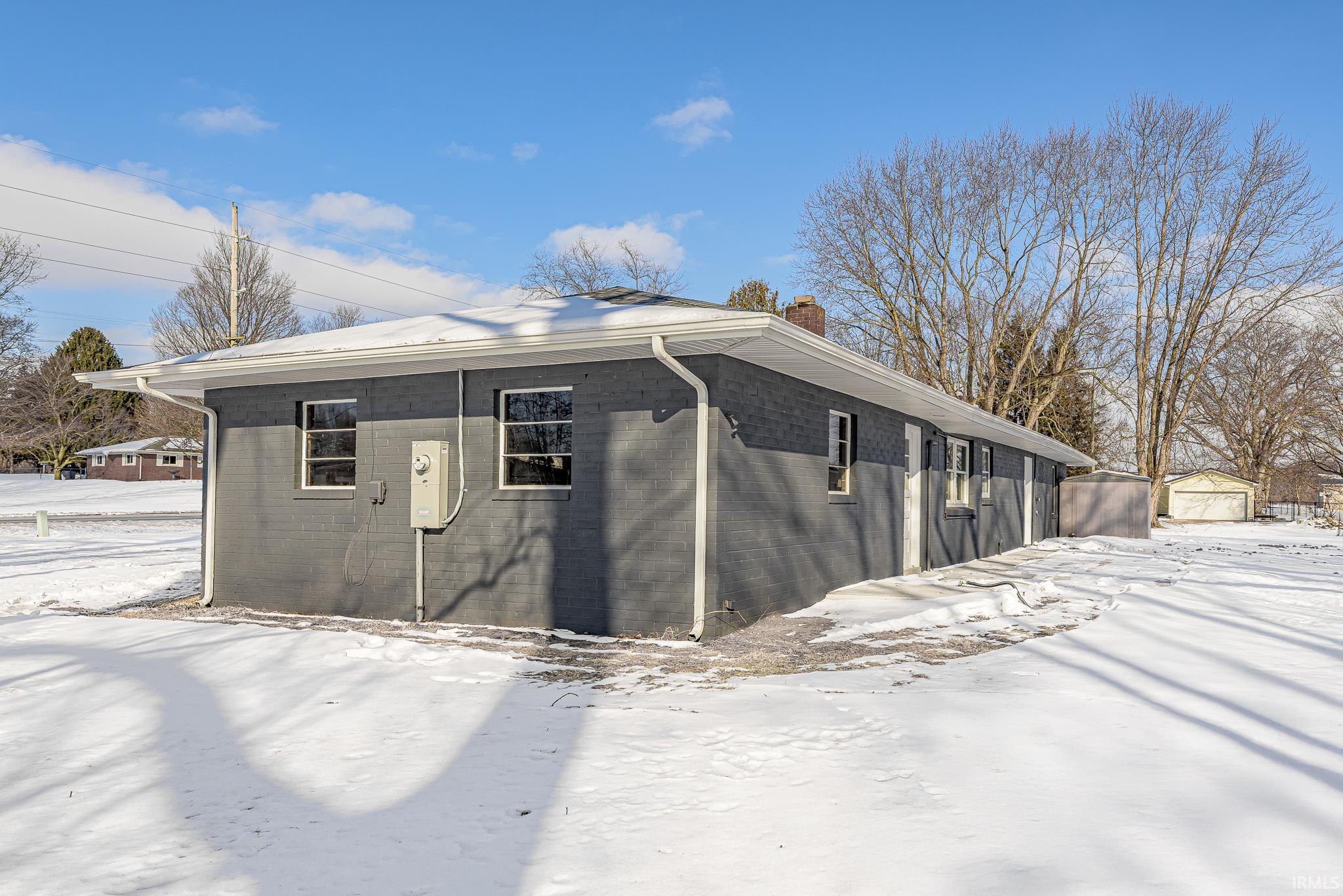 View of snow covered exterior with an outdoor structure, a chimney, and brick siding