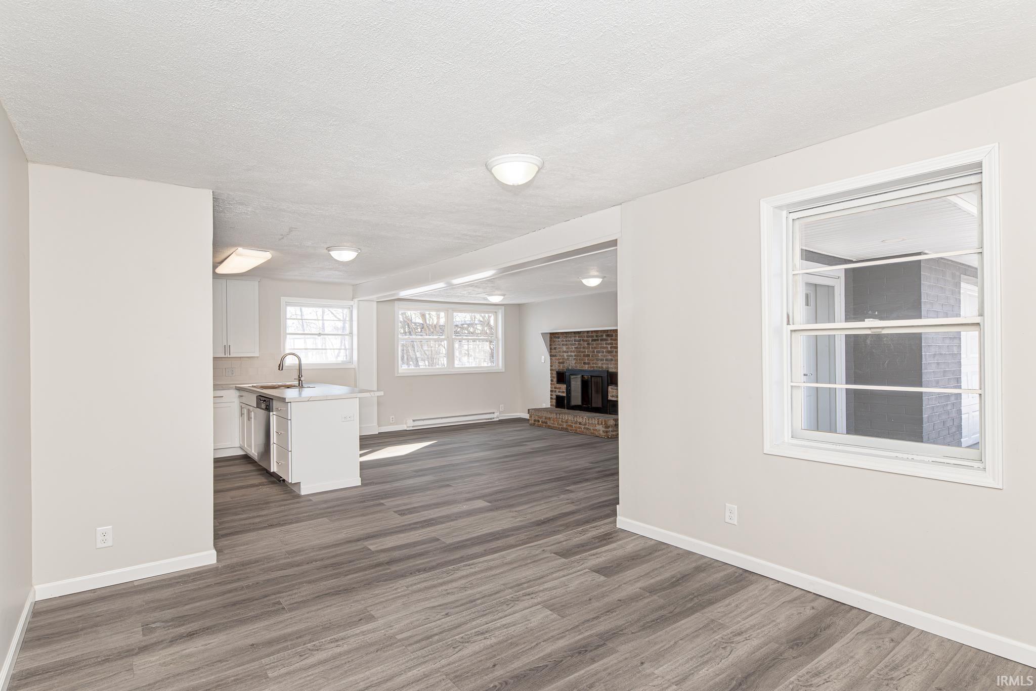 Unfurnished living room with wood finished floors, a fireplace, baseboard heating, and a textured ceiling