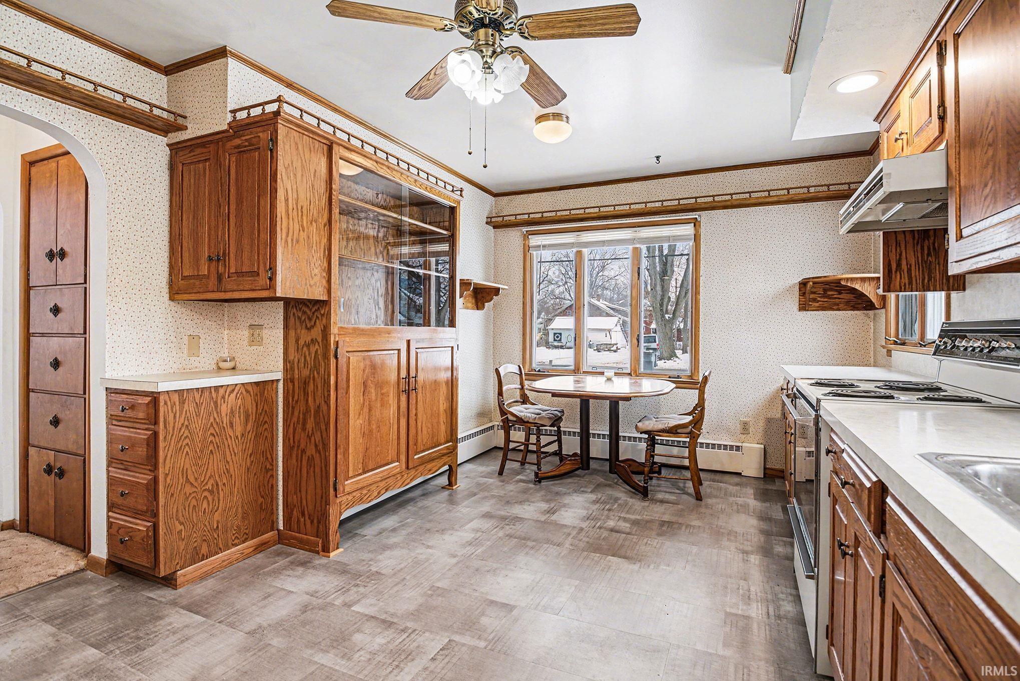Kitchen featuring wallpapered walls, light countertops, white range with electric stovetop, wood finish cabinets, and light flooring
