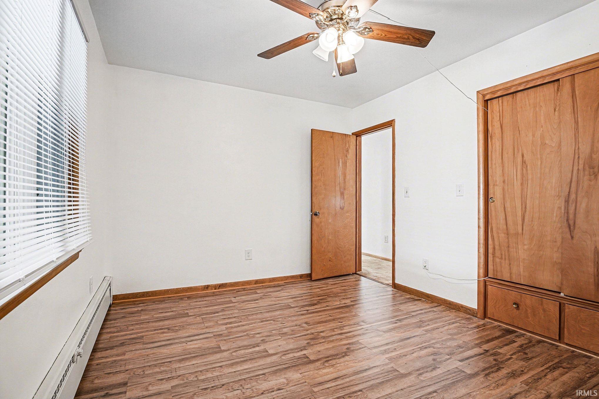 Unfurnished bedroom with a baseboard radiator, wood finished floors, ceiling fan, and a closet