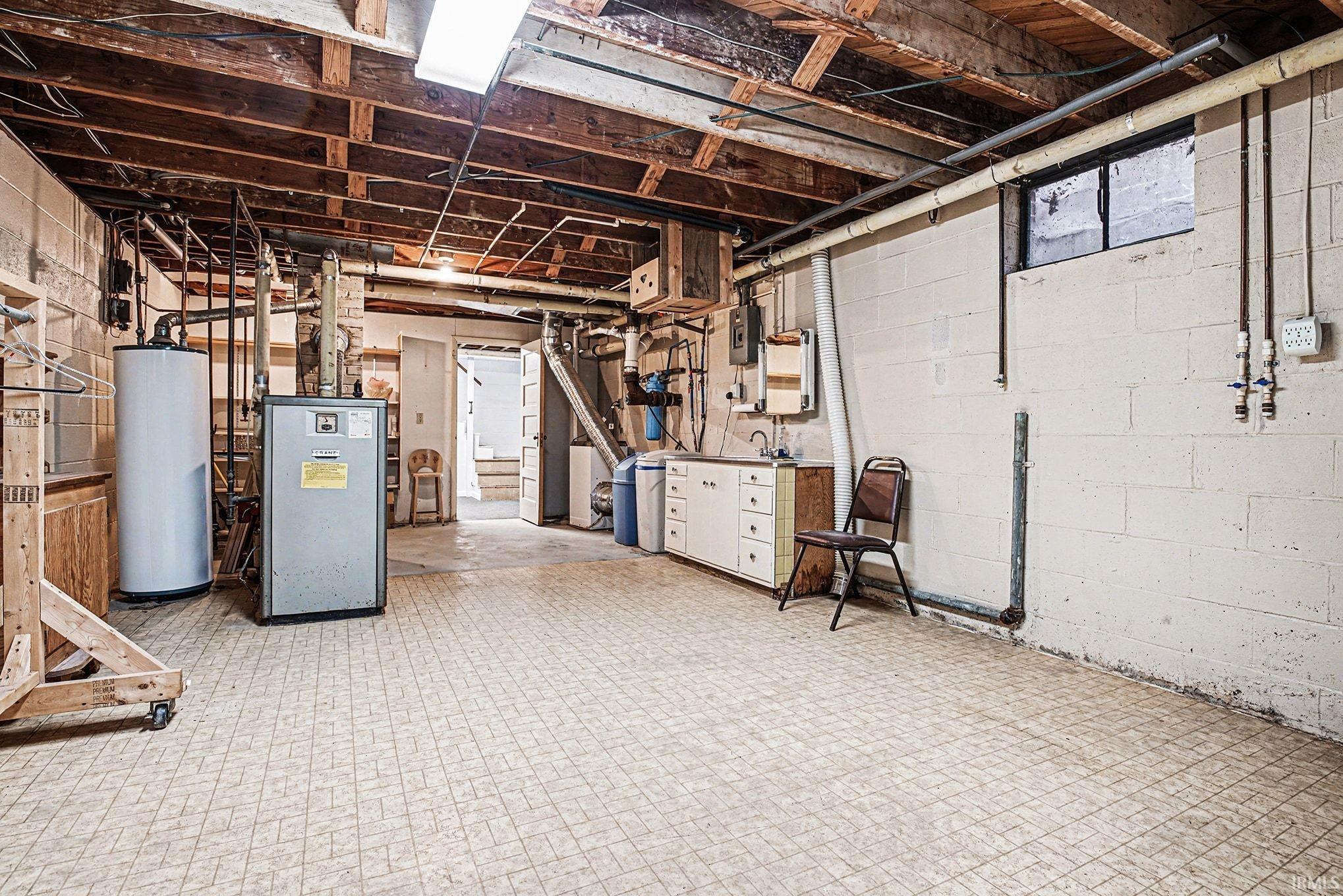 Unfinished below grade area with water heater, a heating unit, and tile patterned floors