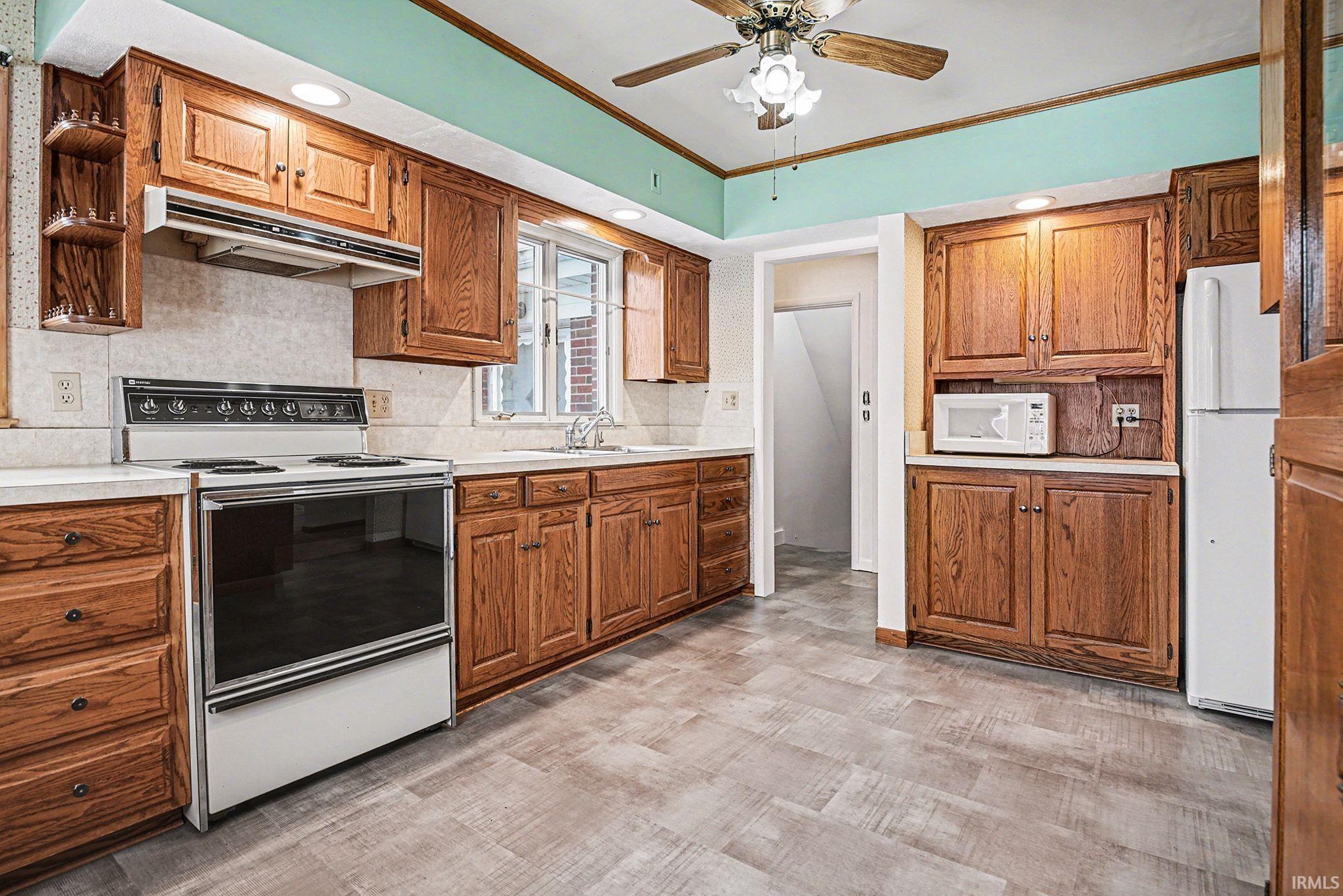 Kitchen with crown molding, white appliances, ceiling fan, light countertops, and tasteful backsplash