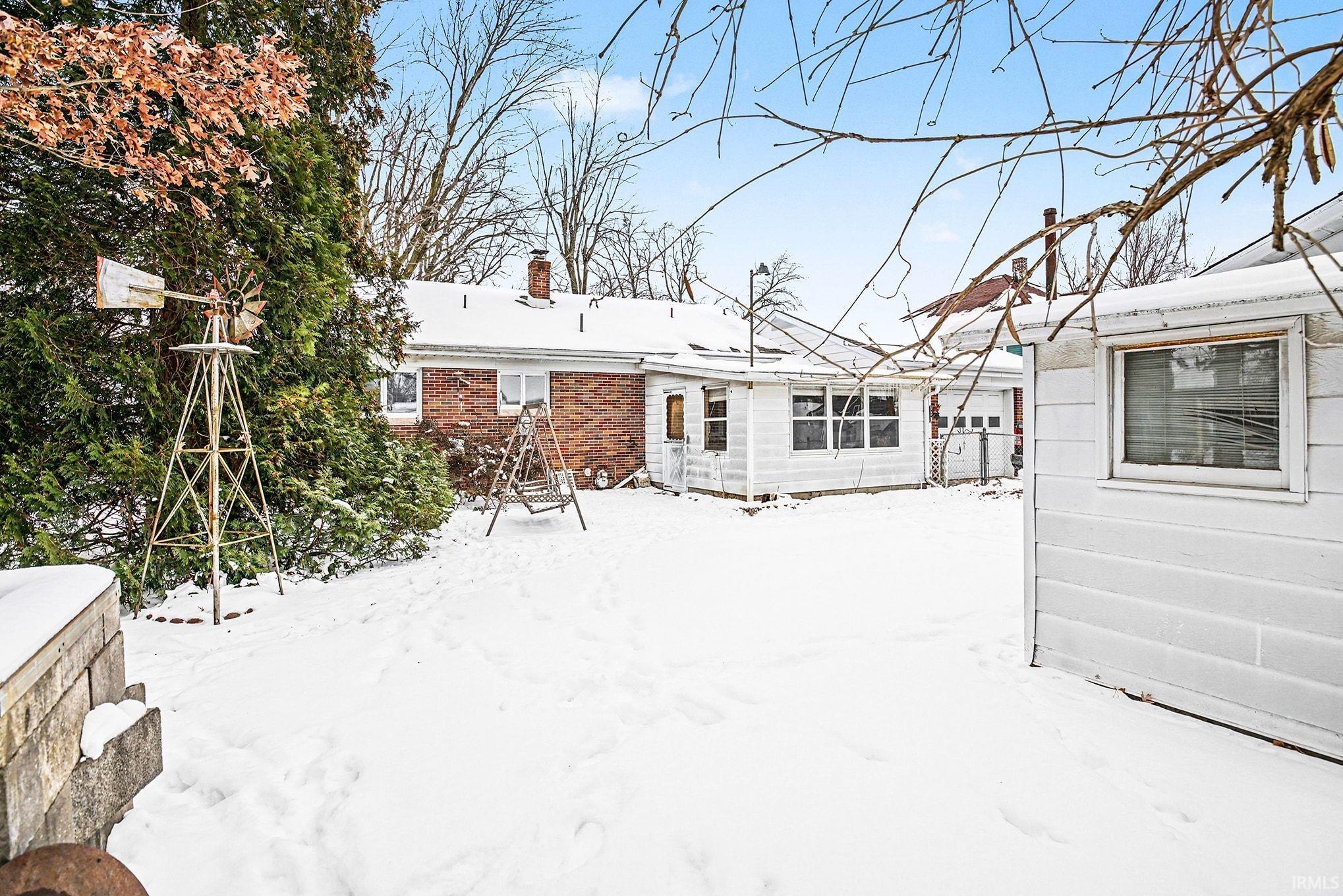 Snow covered rear of property with a chimney and brick siding