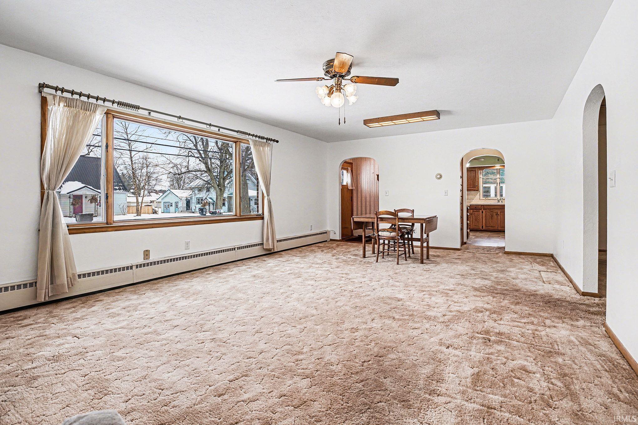 Unfurnished room with a baseboard radiator, ceiling fan, light carpet, and healthy amount of natural light