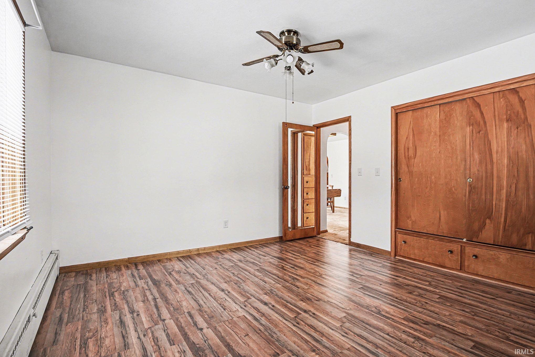Unfurnished bedroom with a baseboard heating unit, dark wood-style floors, a ceiling fan, and a closet