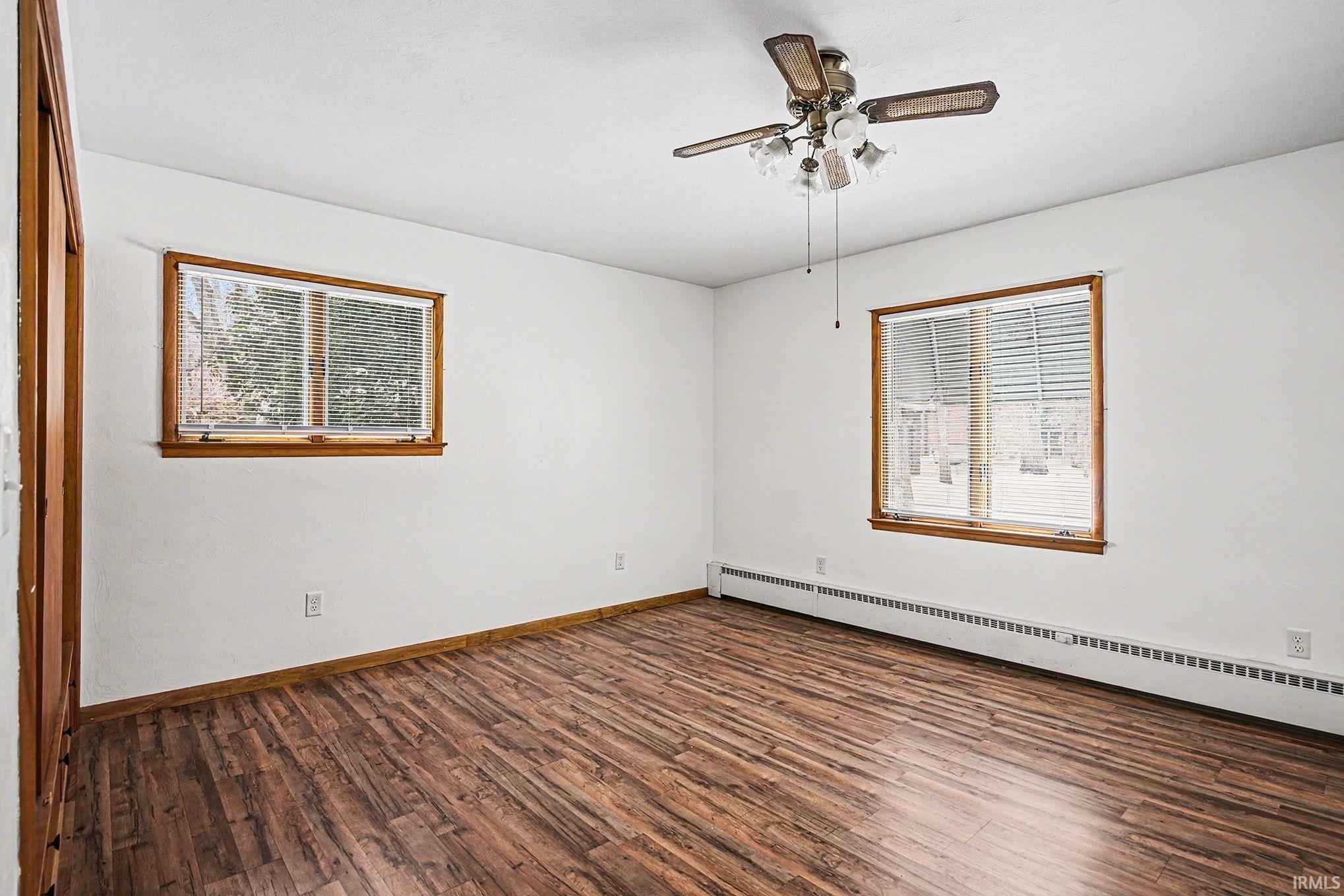 Empty room featuring baseboard heating, dark wood finished floors, plenty of natural light, and a ceiling fan