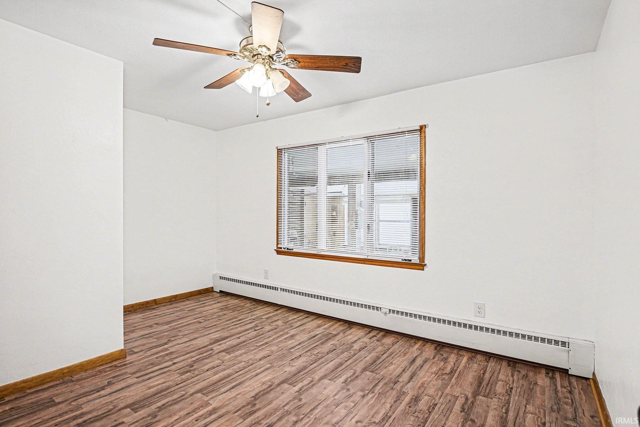 Unfurnished room featuring baseboard heating, wood finished floors, and ceiling fan