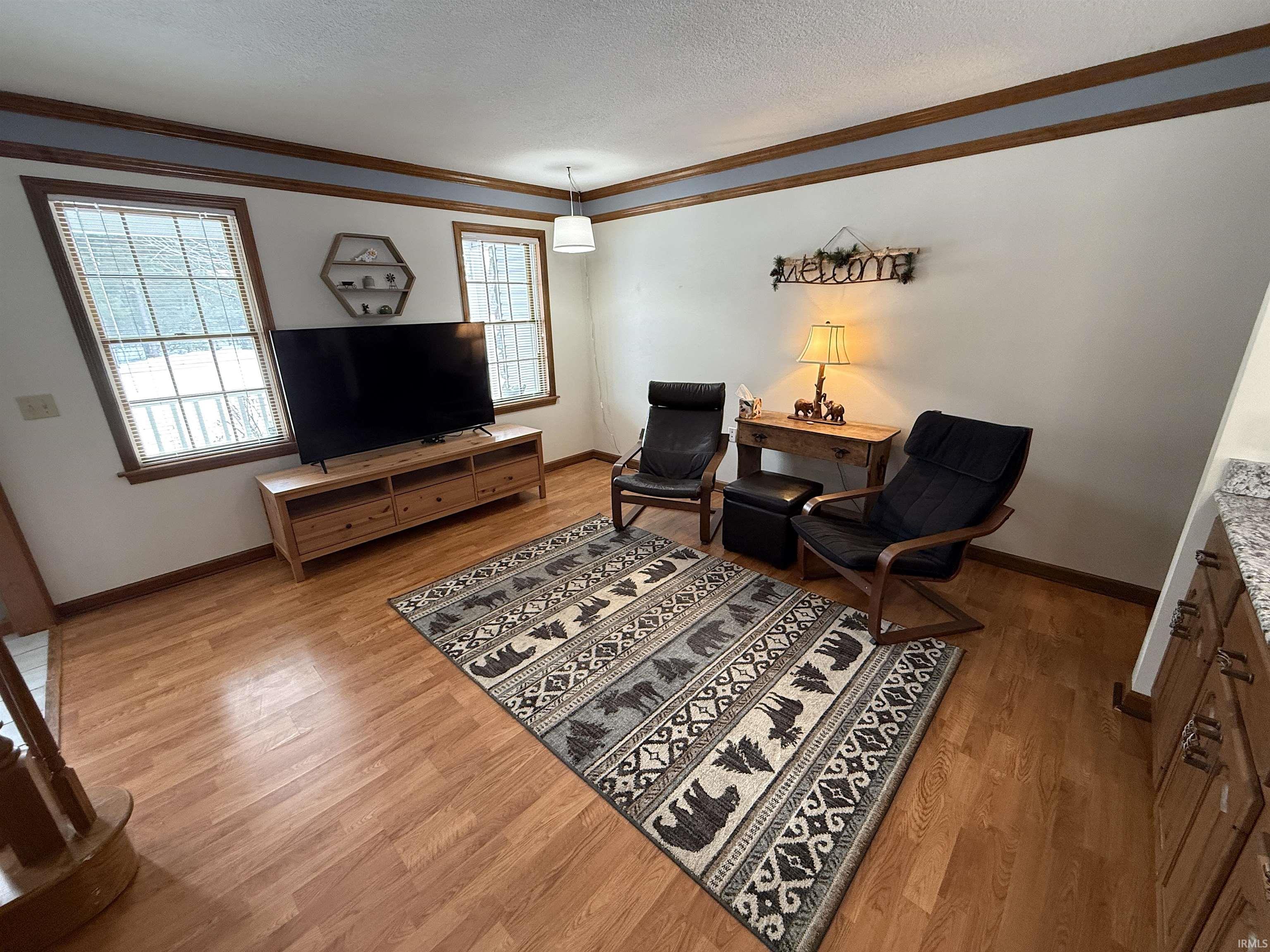 Sitting room with light wood-type flooring, ornamental molding, and a textured ceiling