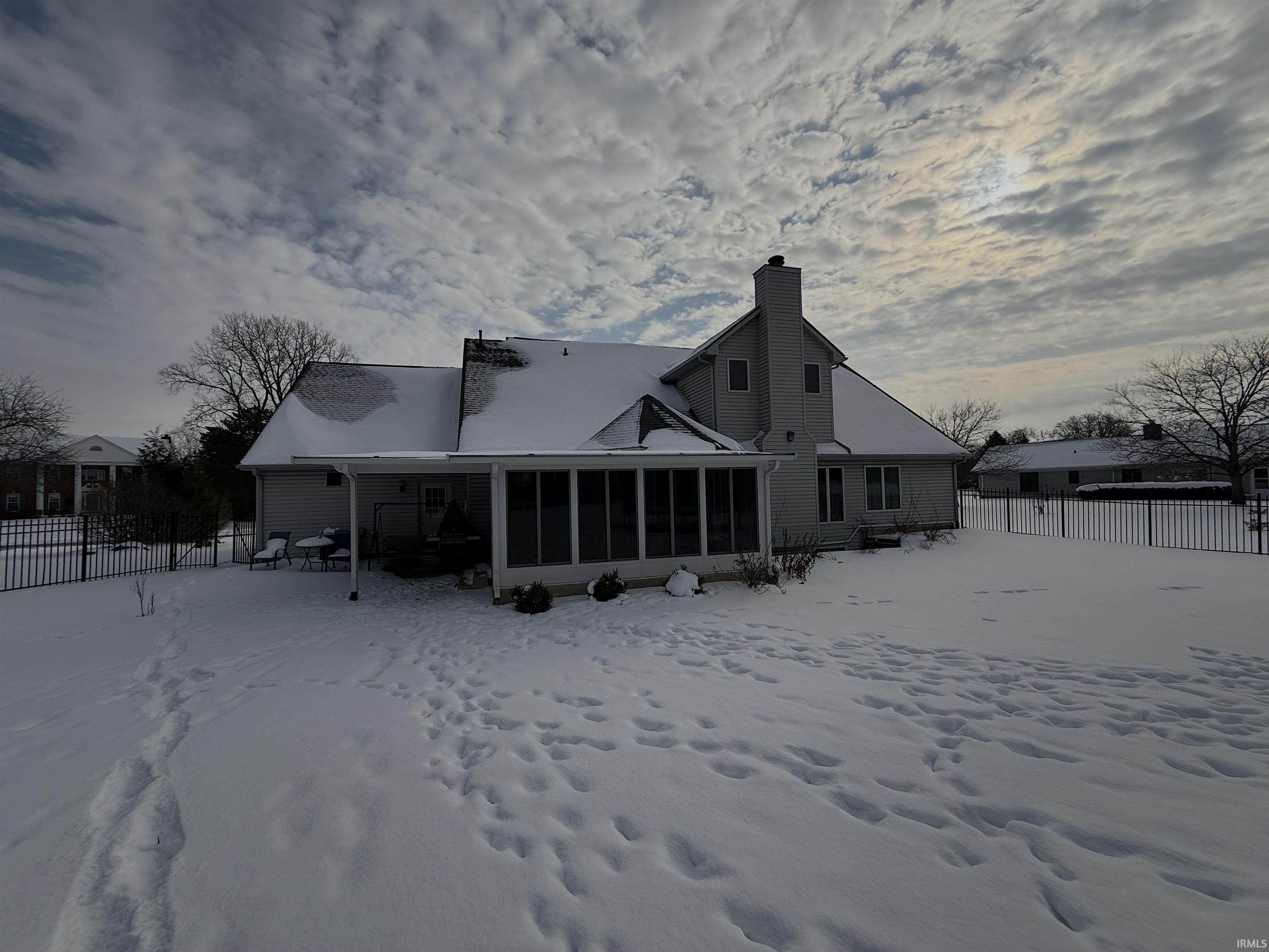 Snow covered back of property with a chimney and a sunroom