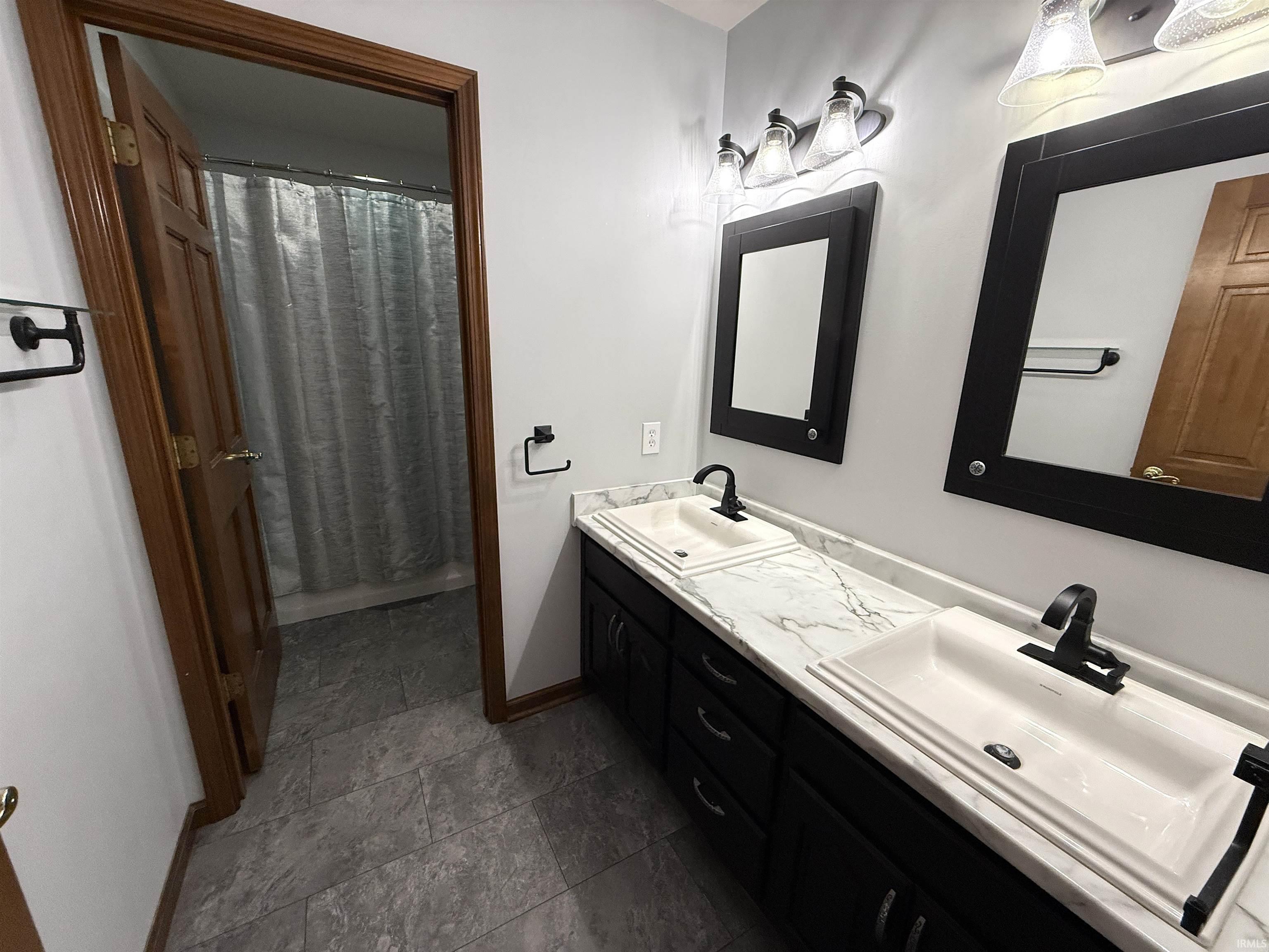 Full bath with double vanity and dark stone finish floors
