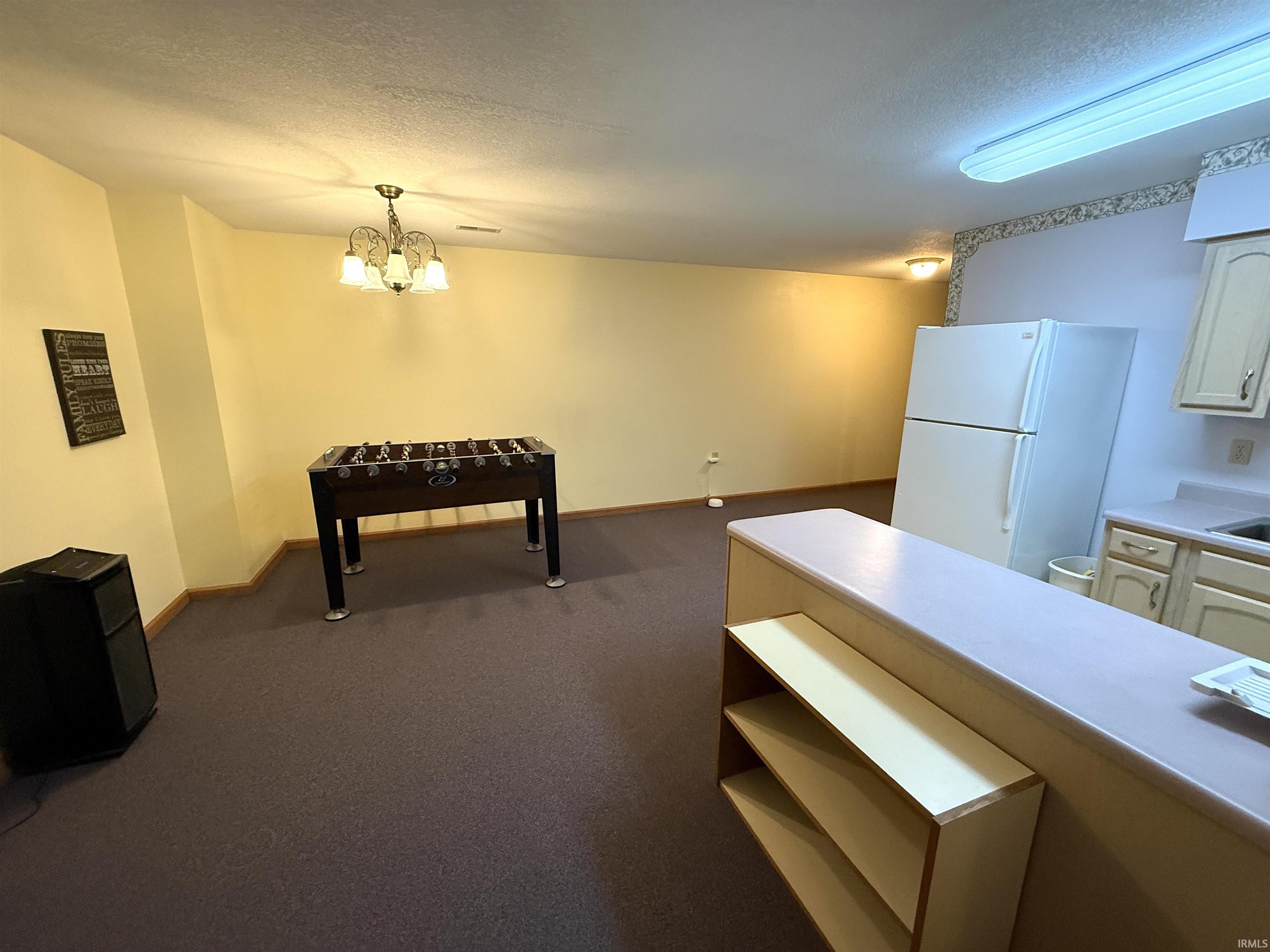 Kitchen with freestanding refrigerator, a textured ceiling, light countertops, dark carpet, and hanging lights
