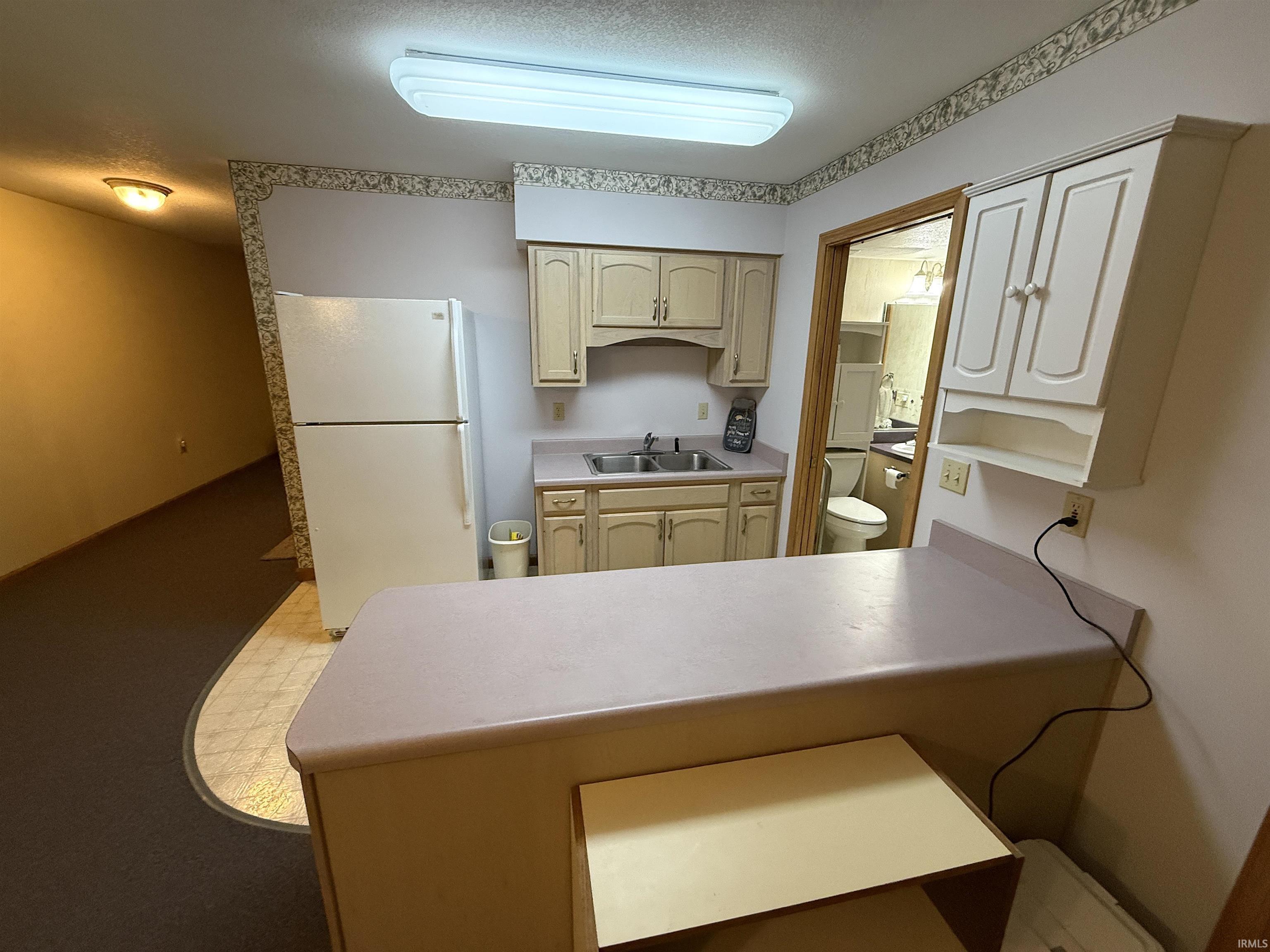 Kitchen featuring freestanding refrigerator, light countertops, a peninsula, and a textured ceiling