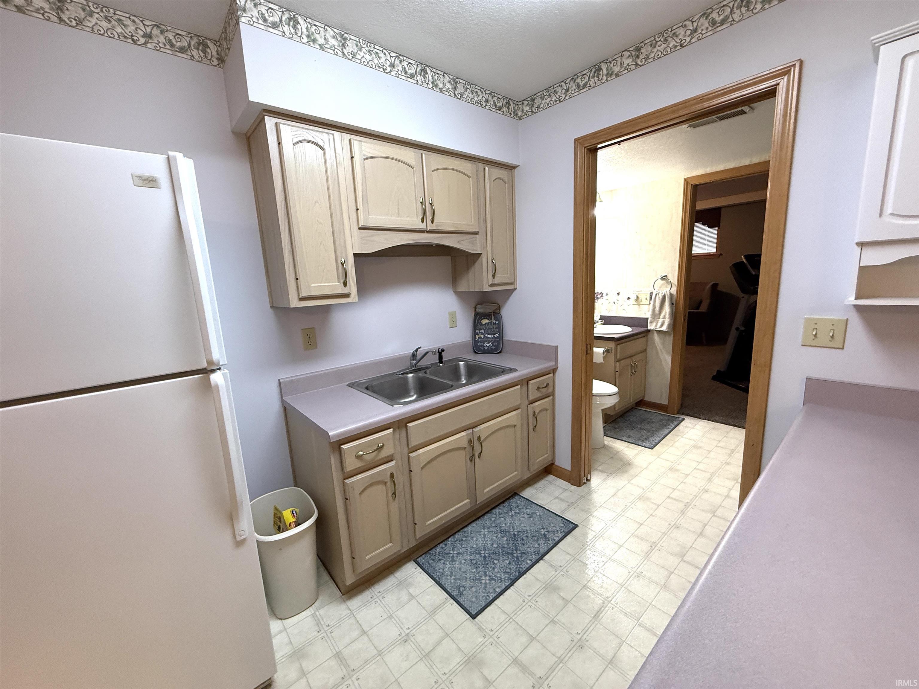 Kitchen featuring light flooring, freestanding refrigerator, light countertops, and light wood finish cabinets