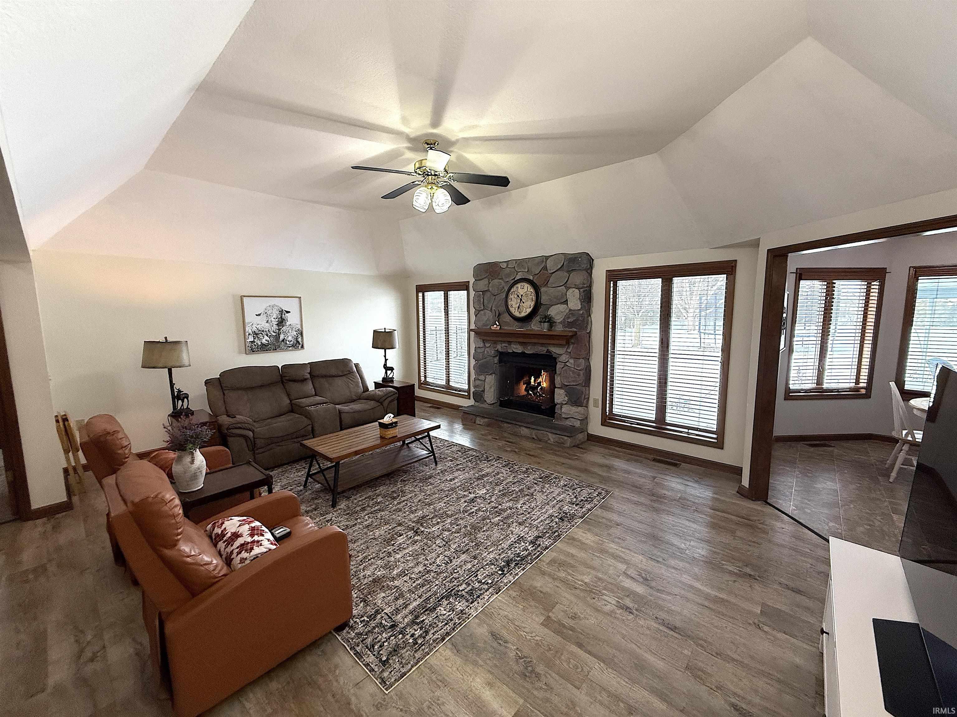 Living room with ceiling fan, lofted ceiling, wood finished floors, and a fireplace