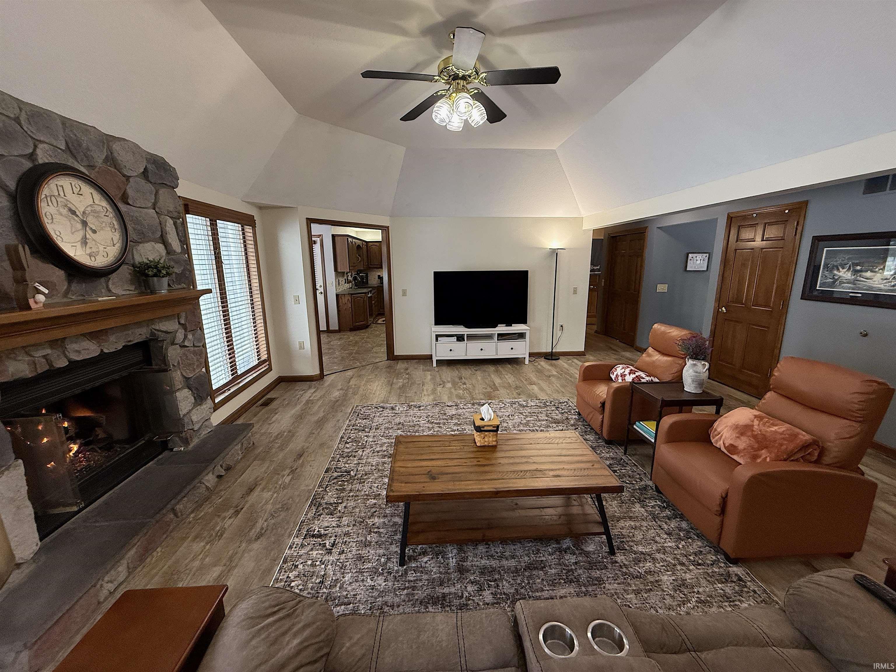 Living room with ceiling fan, a fireplace, lofted ceiling, and wood finished floors