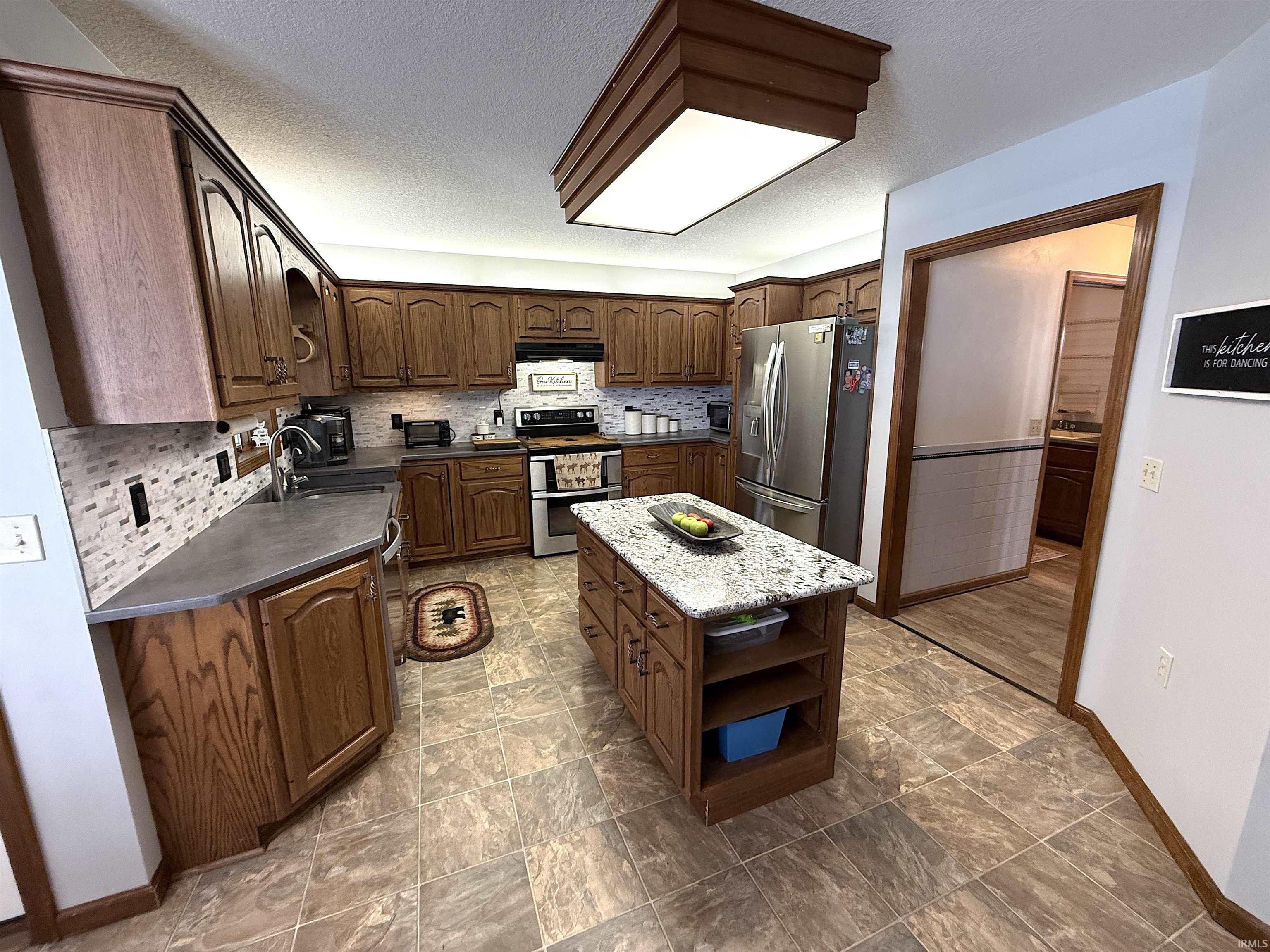 Kitchen featuring stainless steel appliances, dark countertops, a center island, a textured ceiling, and open shelves