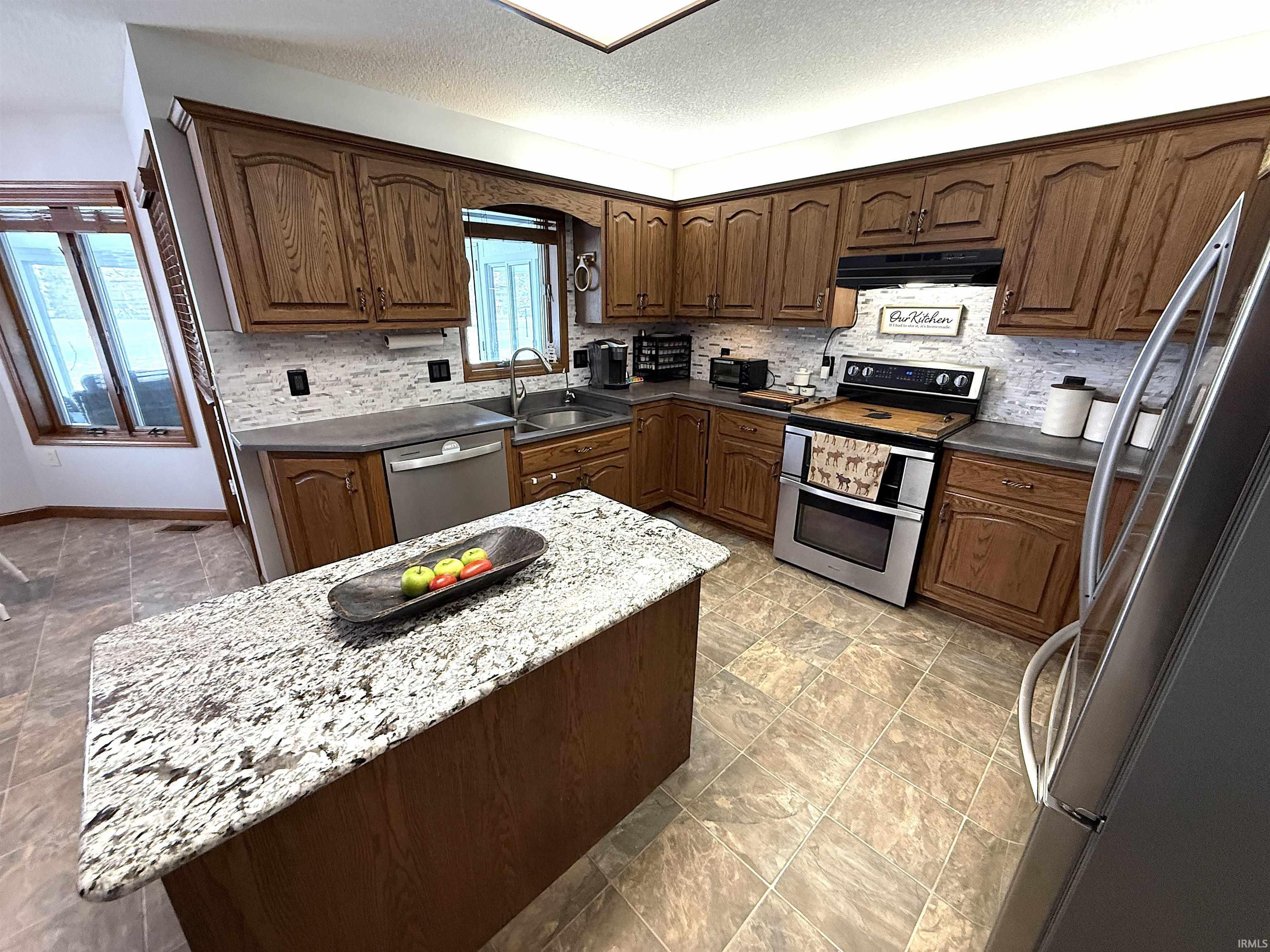 Kitchen featuring tasteful backsplash, stainless steel appliances, dark wood finish cabinetry, a center island, and dark stone countertops