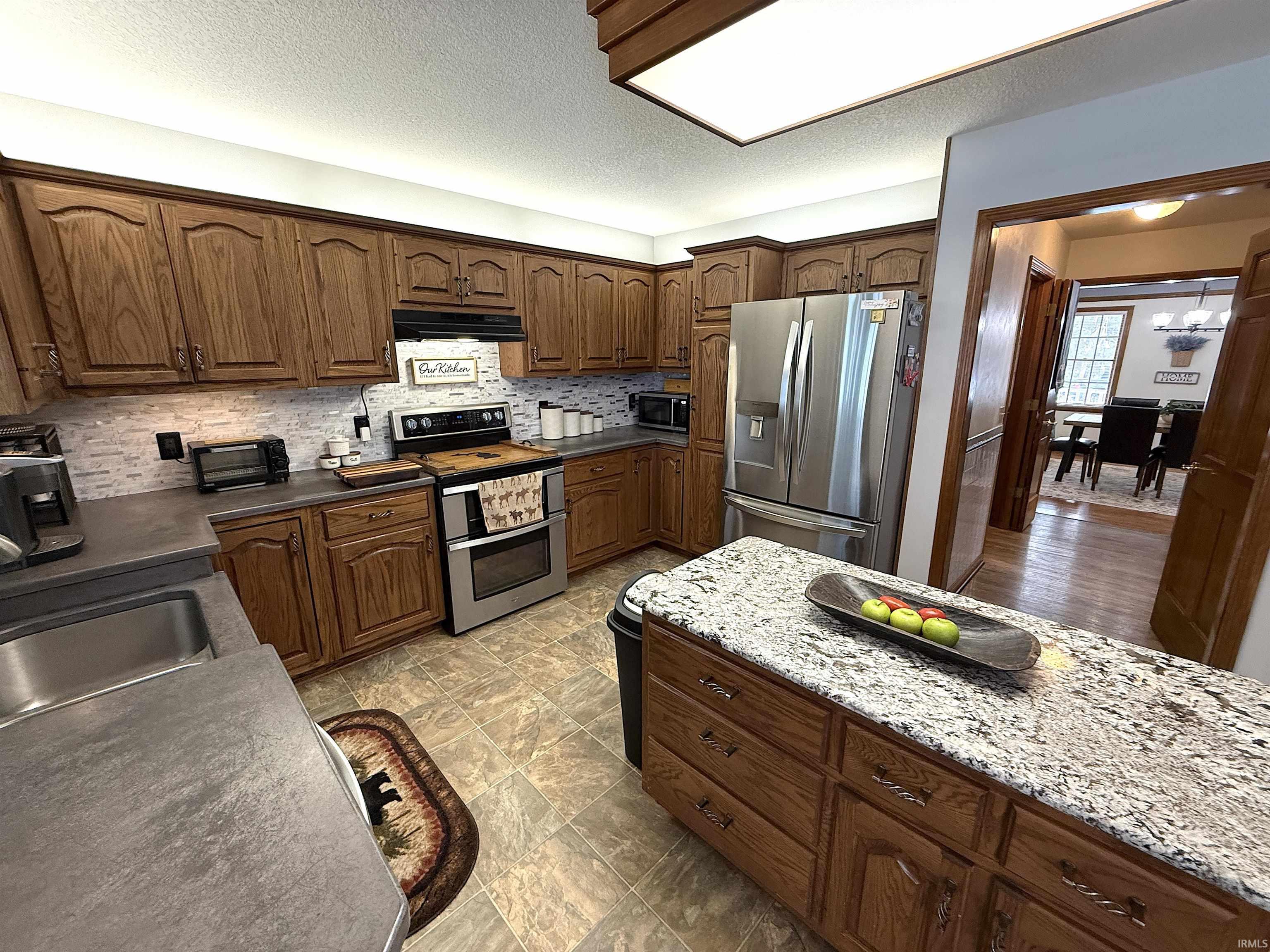 Kitchen with stainless steel appliances, a textured ceiling, dark wood finish cabinetry, dark stone counters, and decorative backsplash