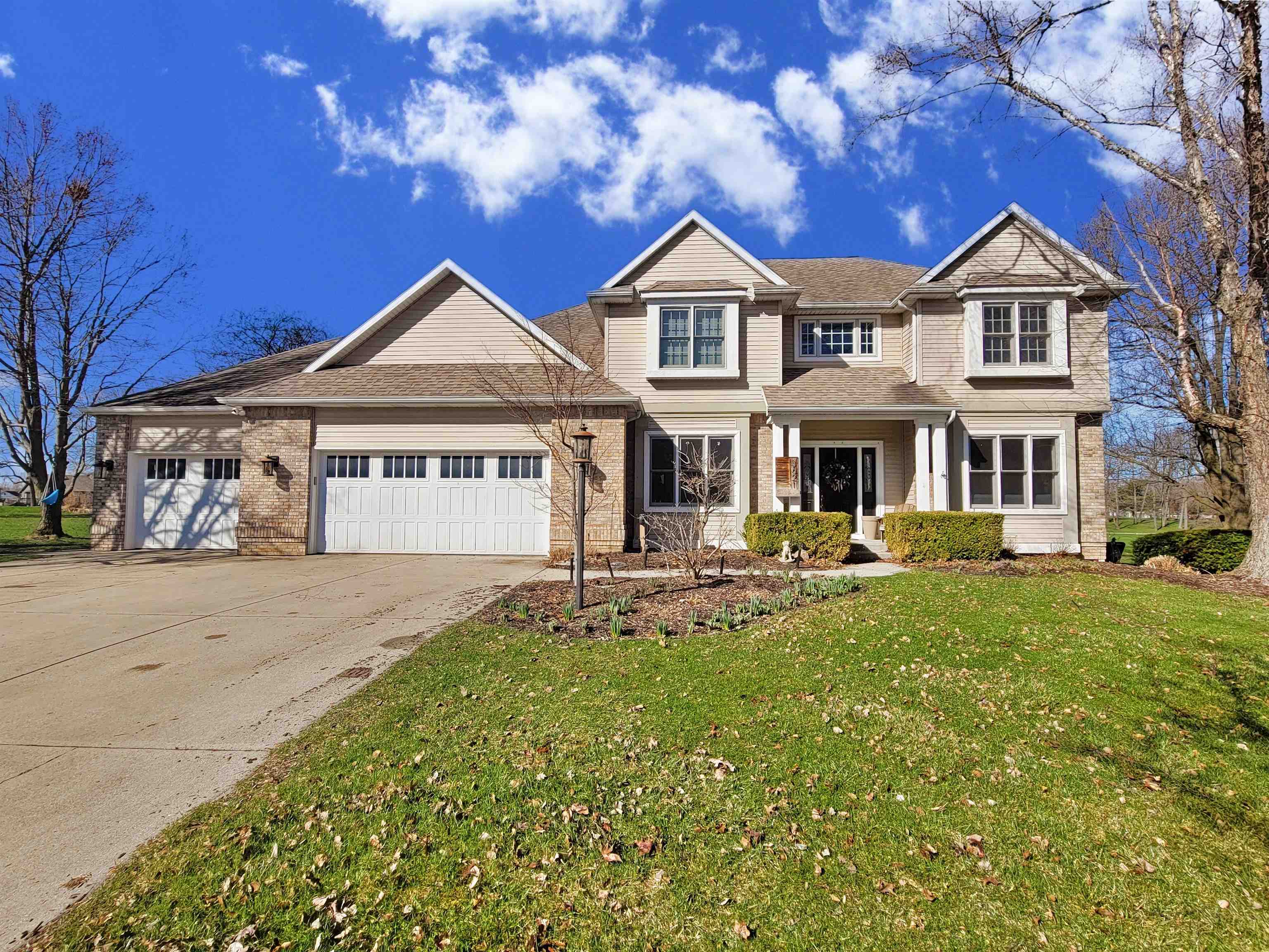 View of front of property with an attached garage, concrete driveway, a front yard, brick siding, and covered porch
