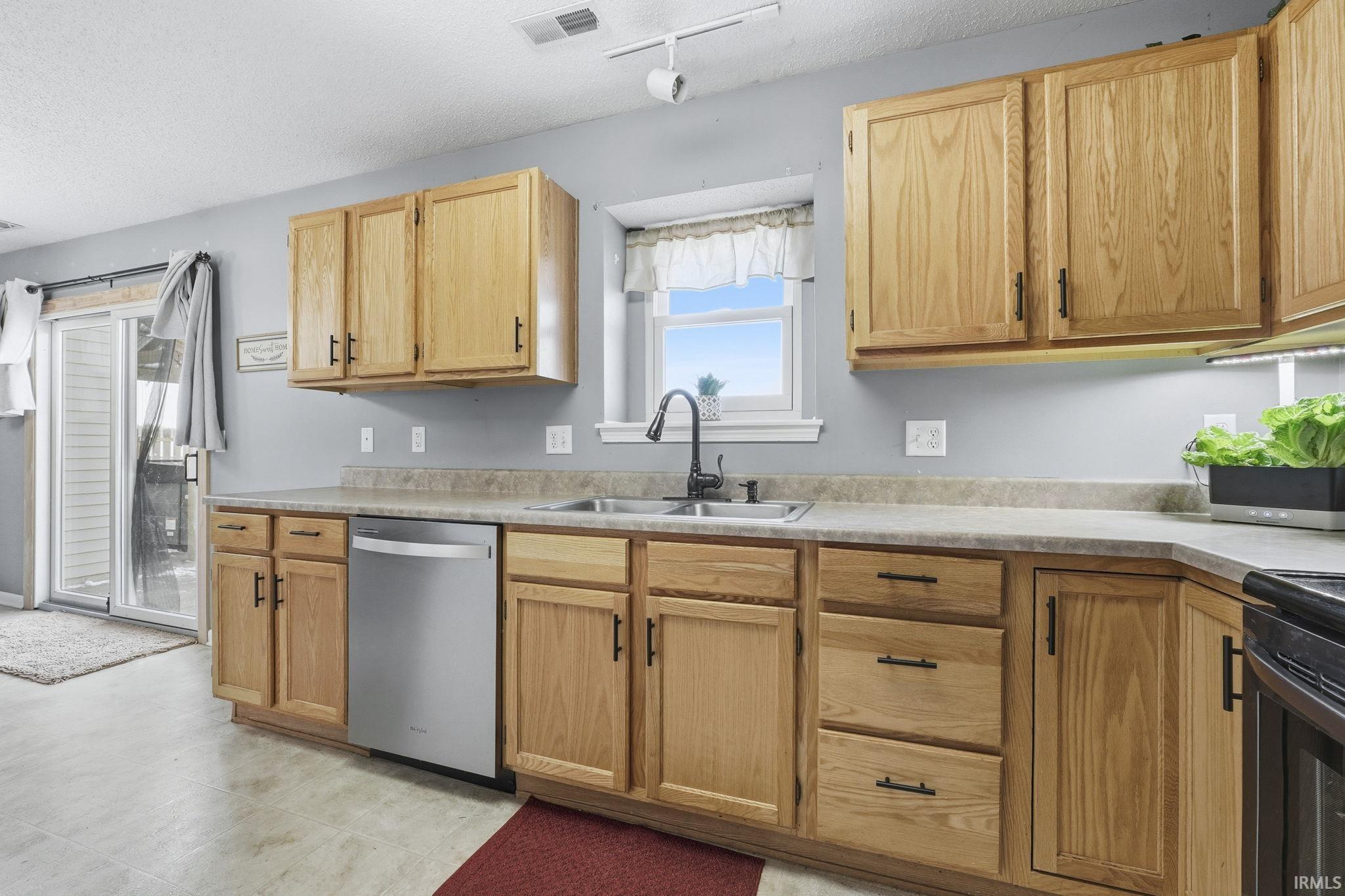 Kitchen featuring light countertops, dishwasher, light wood finish cabinetry, a textured ceiling, and black range