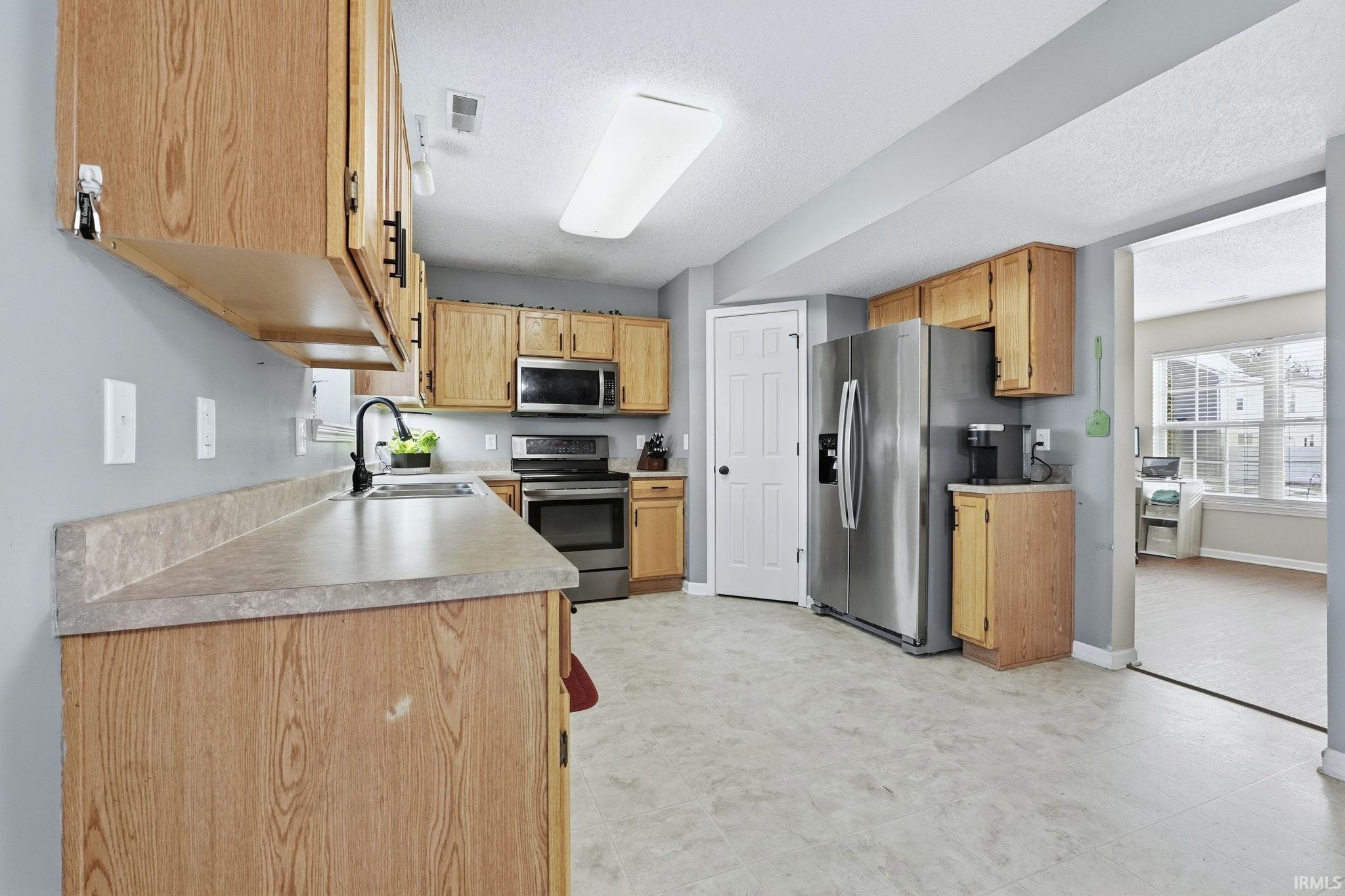 Kitchen with stainless steel appliances, light countertops, light flooring, and a textured ceiling