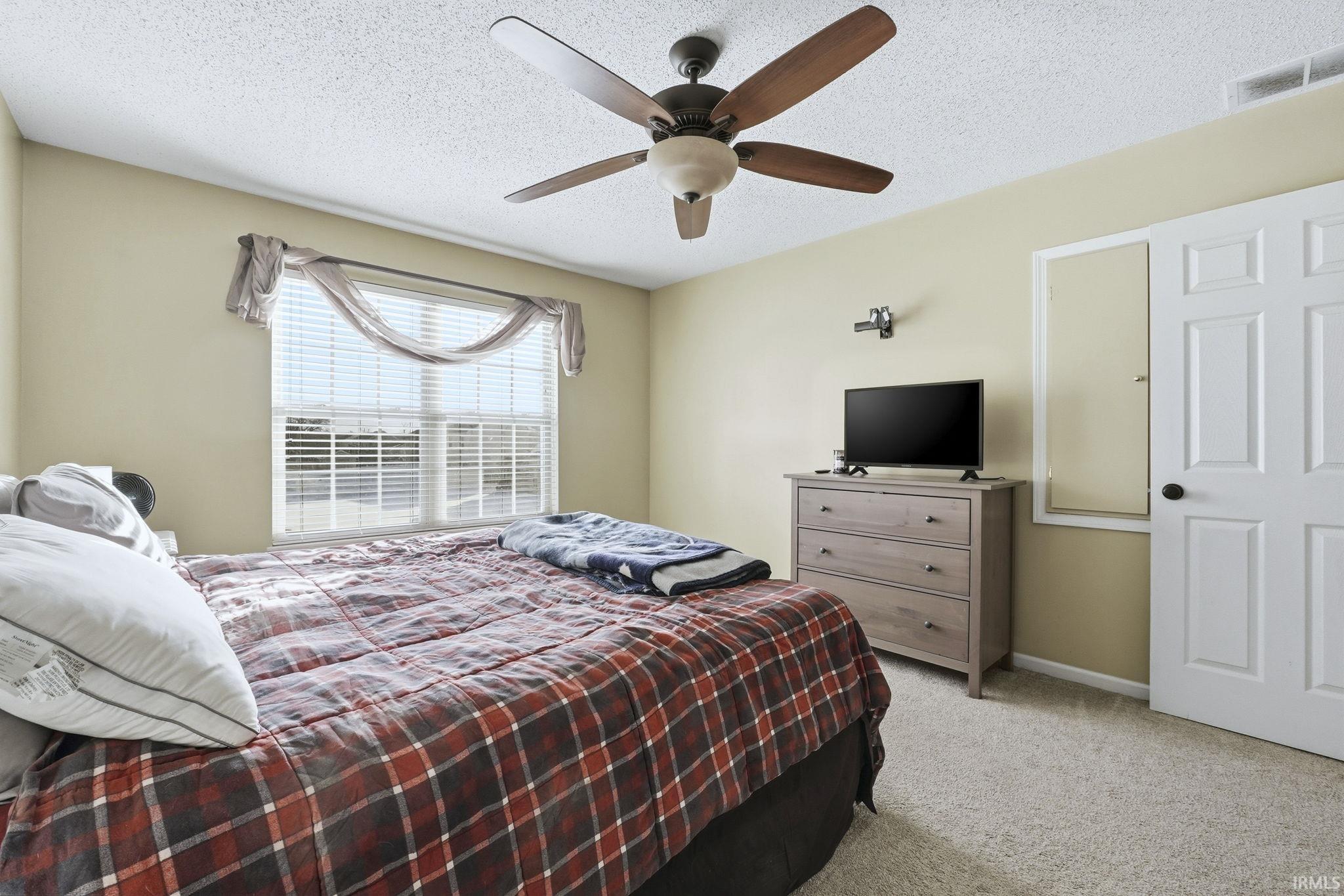 Bedroom with light carpet, a textured ceiling, and a ceiling fan