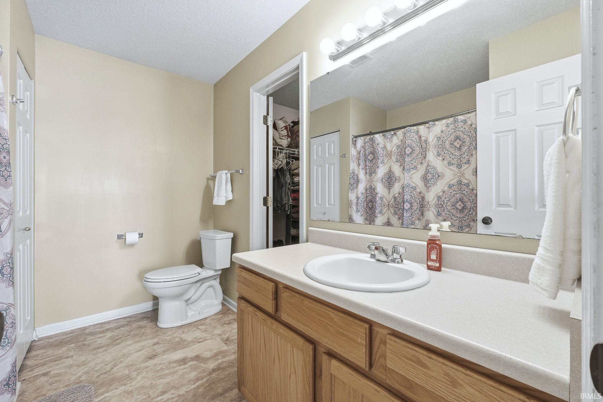 Full bathroom featuring a shower with shower curtain, vanity, a walk in closet, and a textured ceiling