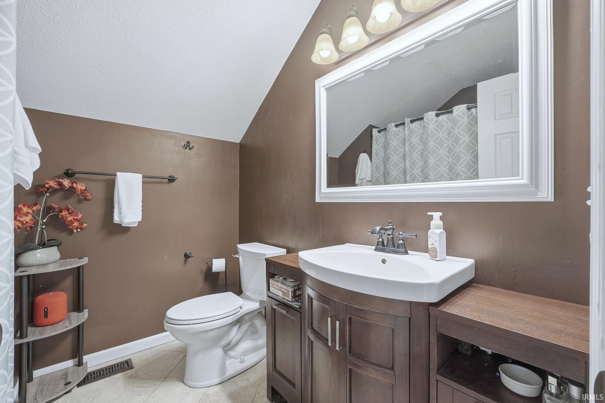 Bathroom featuring vaulted ceiling, vanity, curtained shower, and light tile patterned flooring