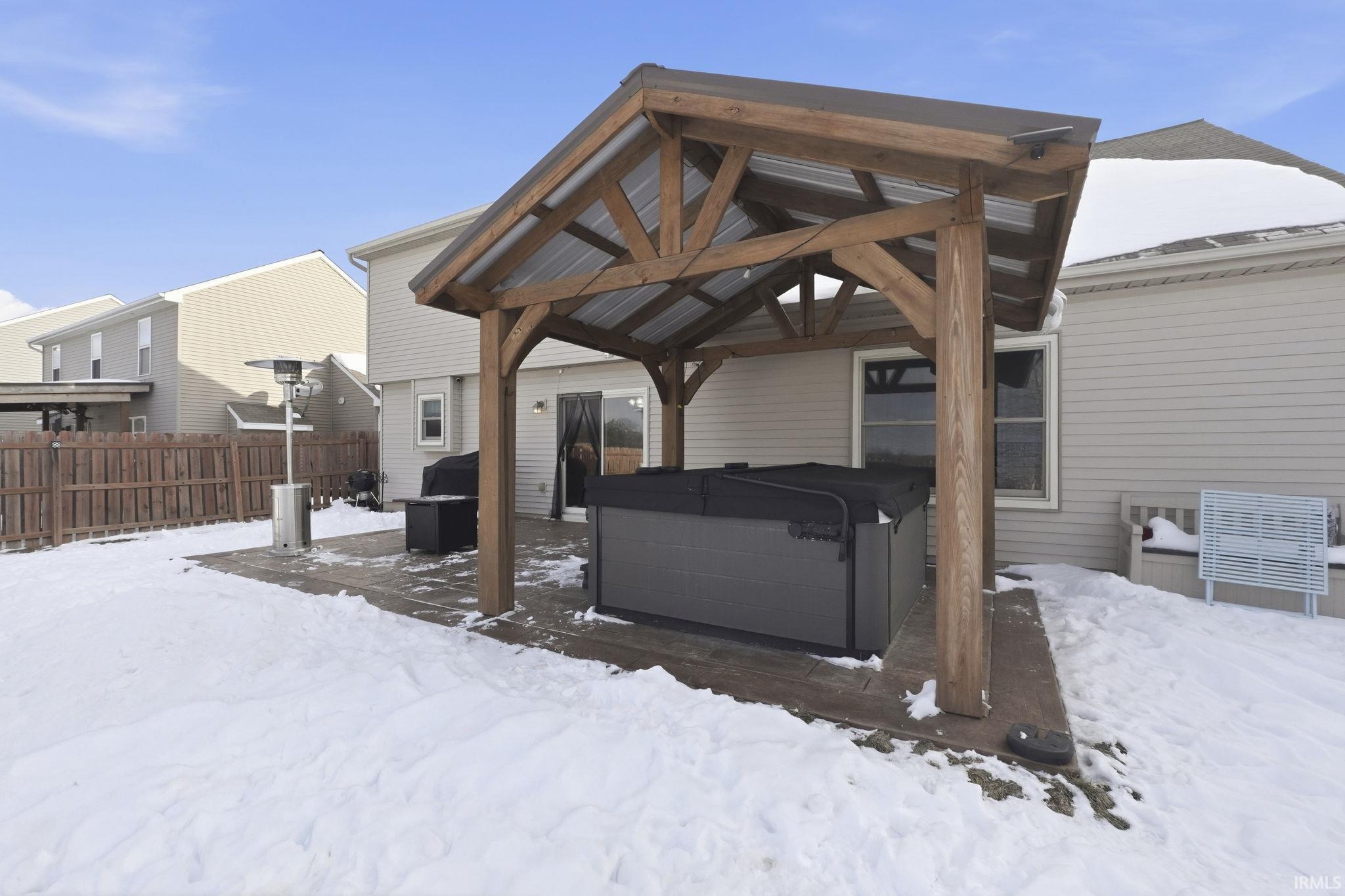 Snow covered back of property with a hot tub, a gazebo, and a patio area