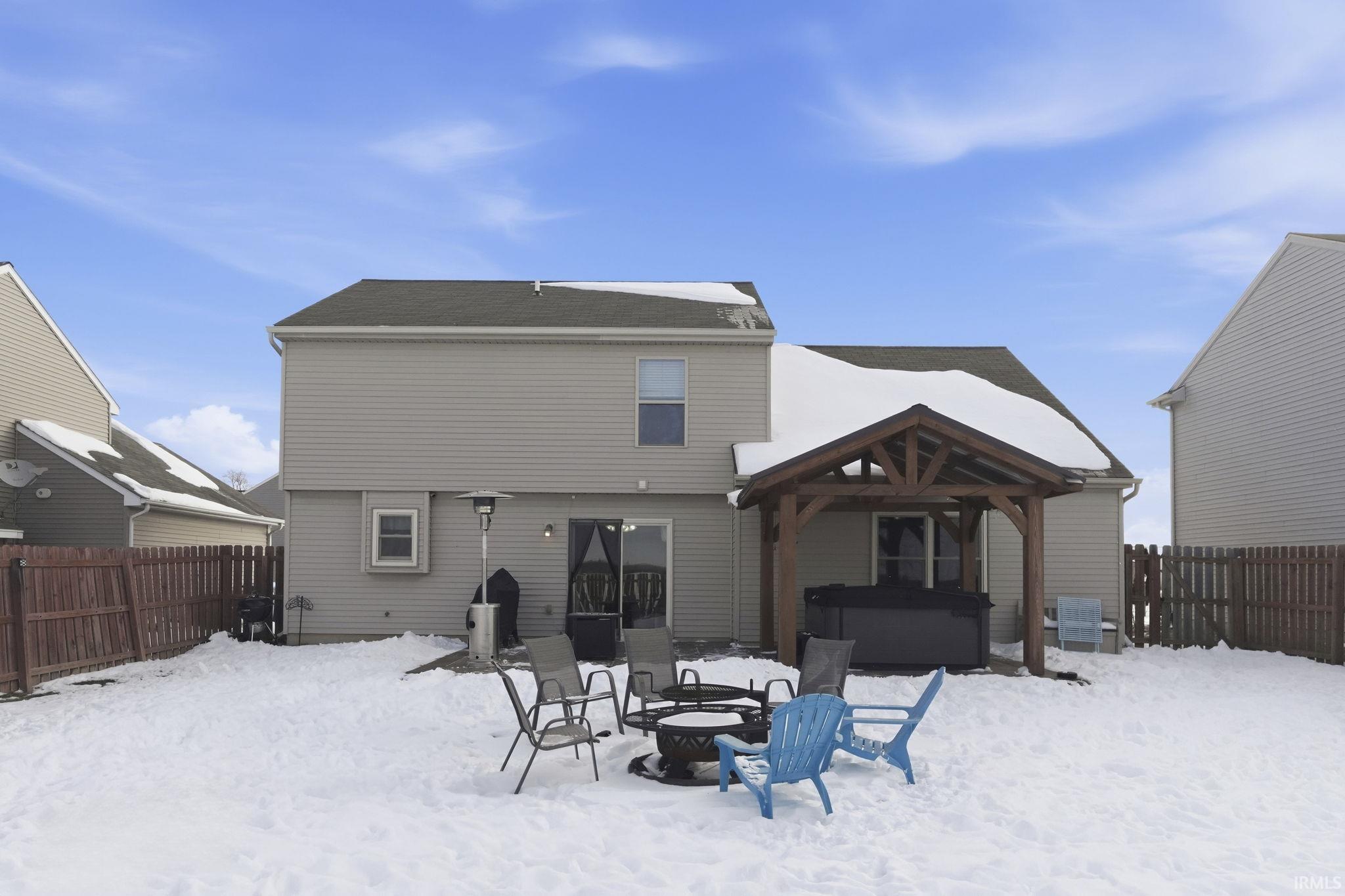 Snow covered rear of property featuring a fenced backyard, a fire pit, a patio, a hot tub, and a gazebo