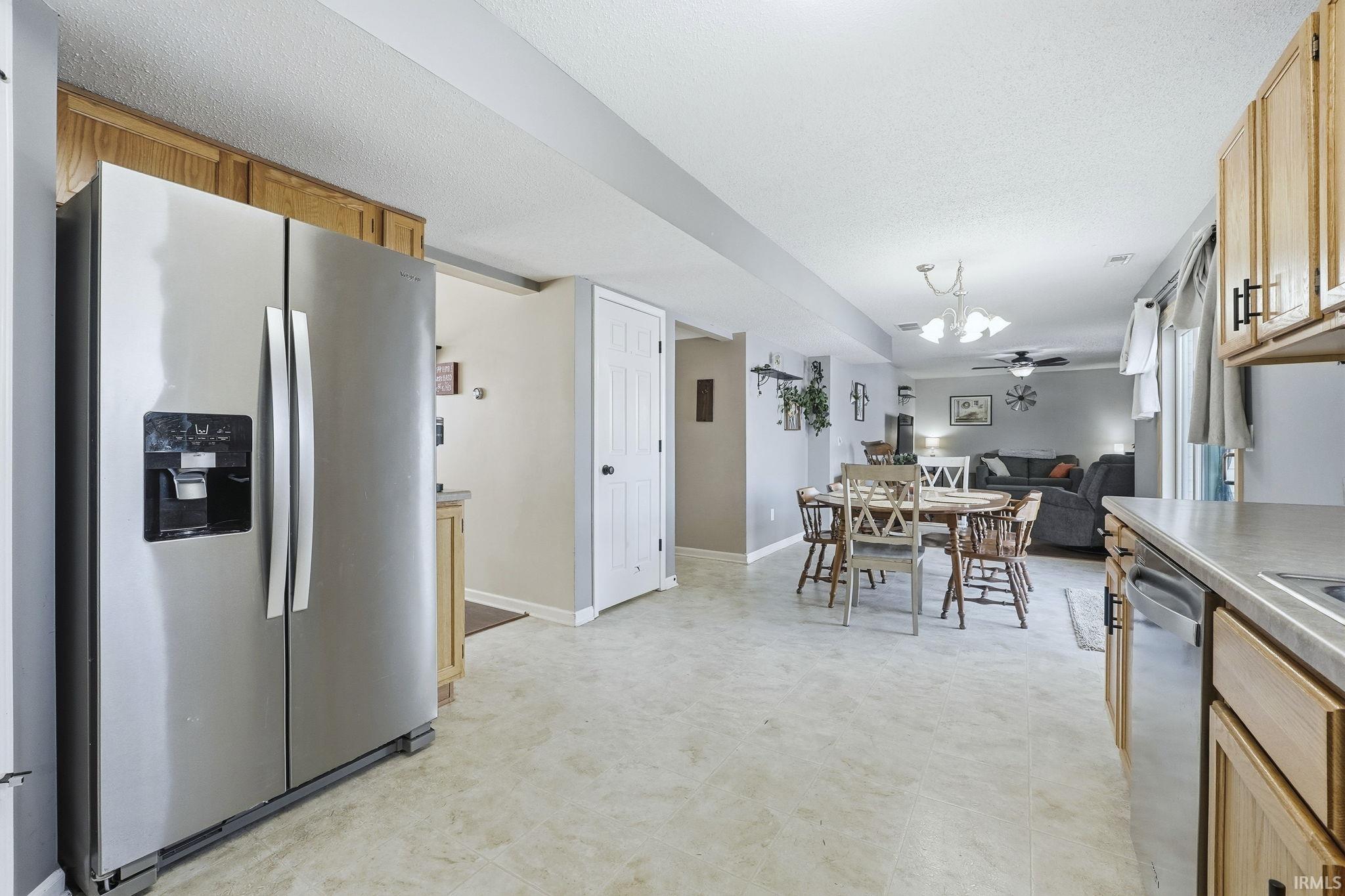 Kitchen featuring stainless steel appliances, light flooring, light wood finish cabinets, a ceiling fan, and a textured ceiling