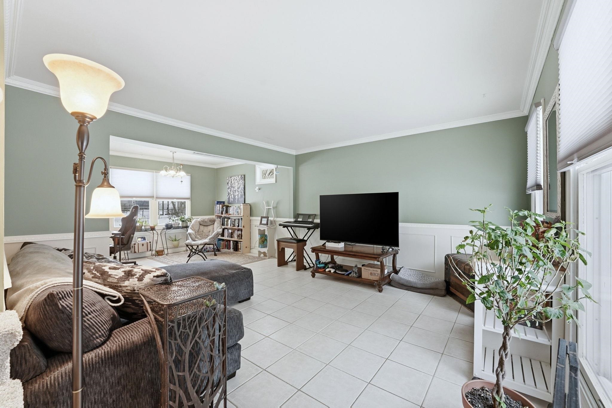 Living area featuring a wainscoted wall, light tile patterned floors, crown molding, a decorative wall, and a chandelier