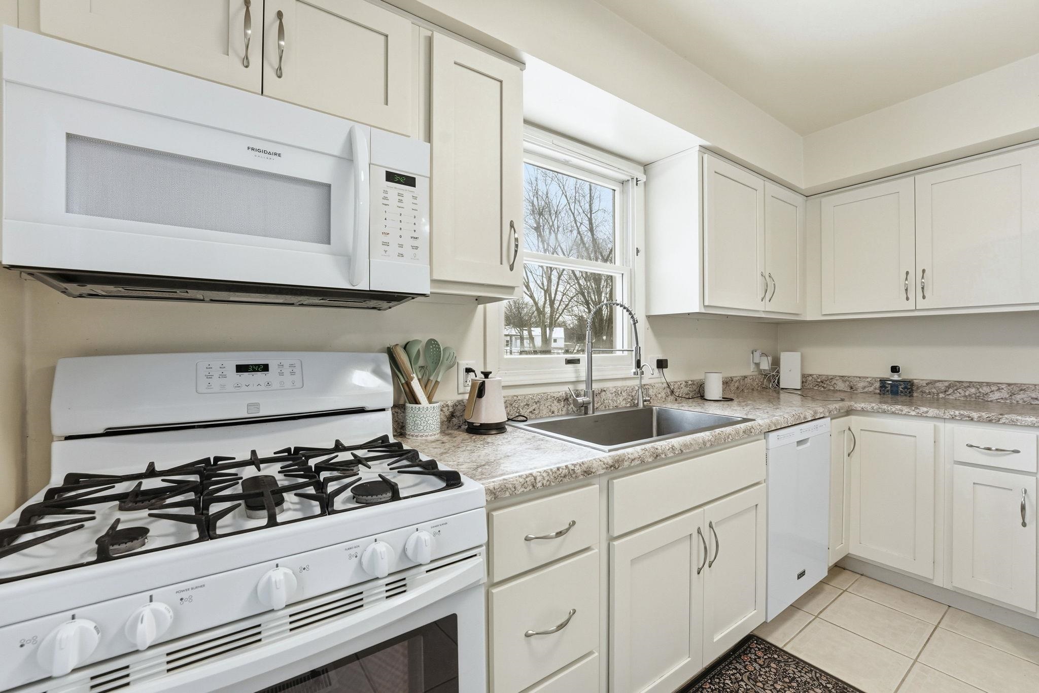 Kitchen featuring white appliances, white cabinets, light countertops, and light tile patterned flooring