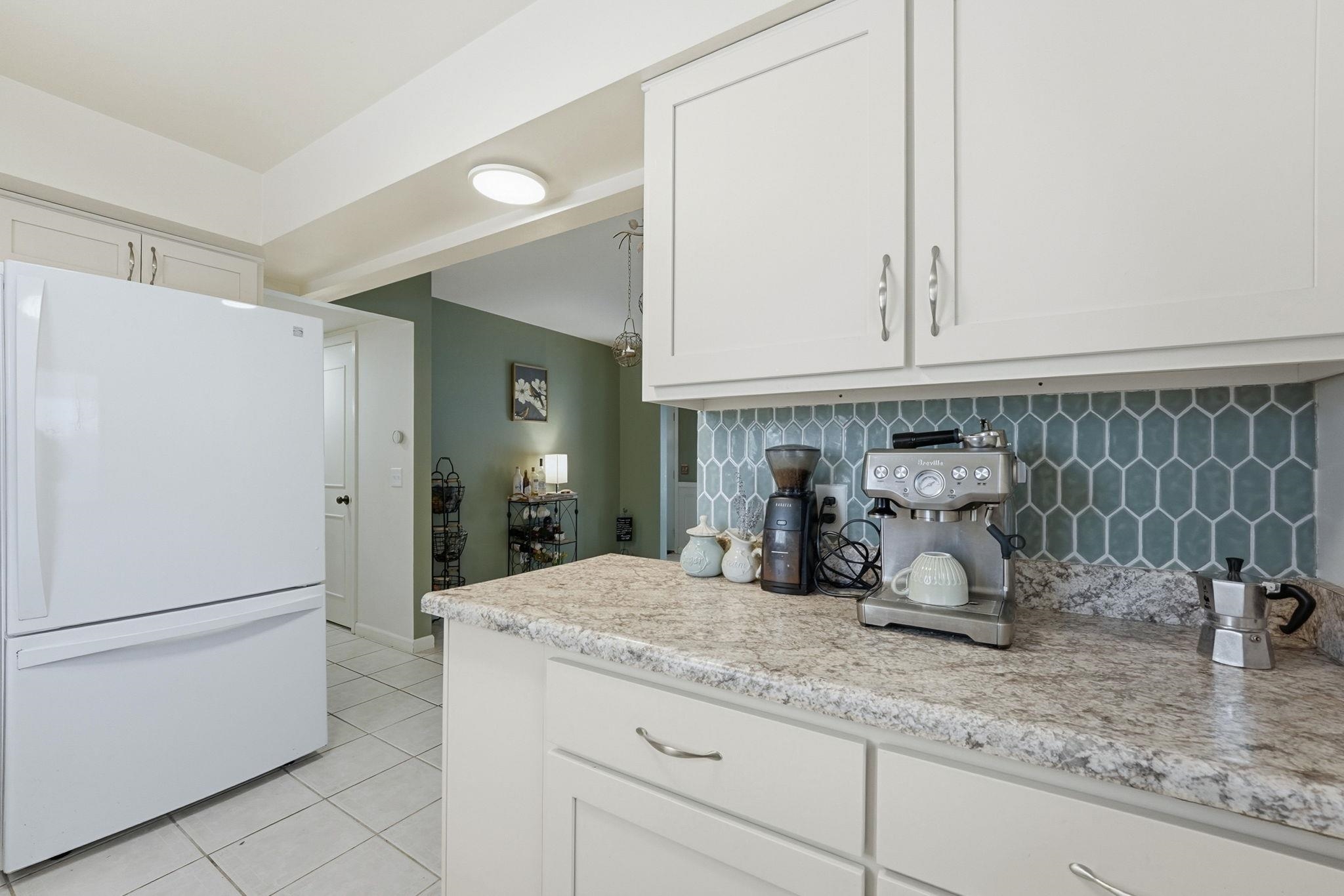 Kitchen featuring freestanding refrigerator, white cabinetry, light tile patterned flooring, and backsplash