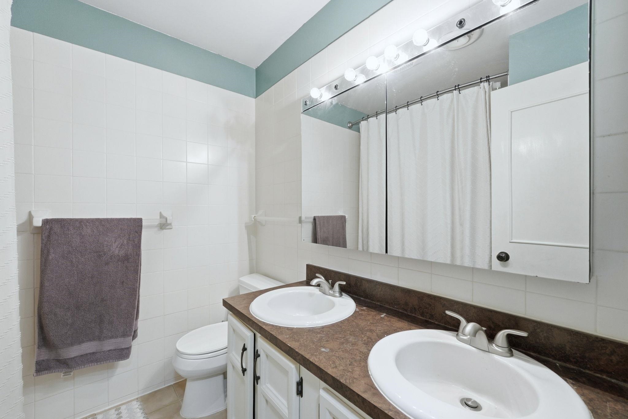 Full bathroom featuring curtained shower, tile walls, double vanity, and backsplash