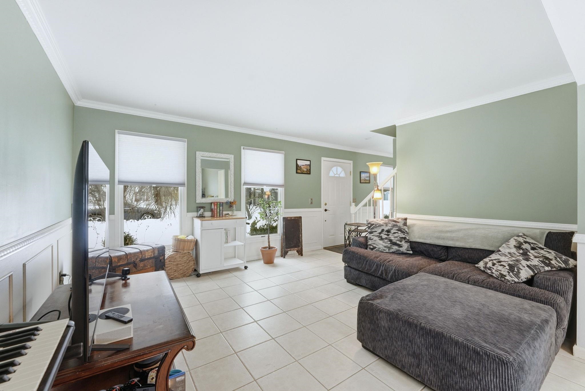 Living room featuring a wainscoted wall, crown molding, tile patterned flooring, and a decorative wall