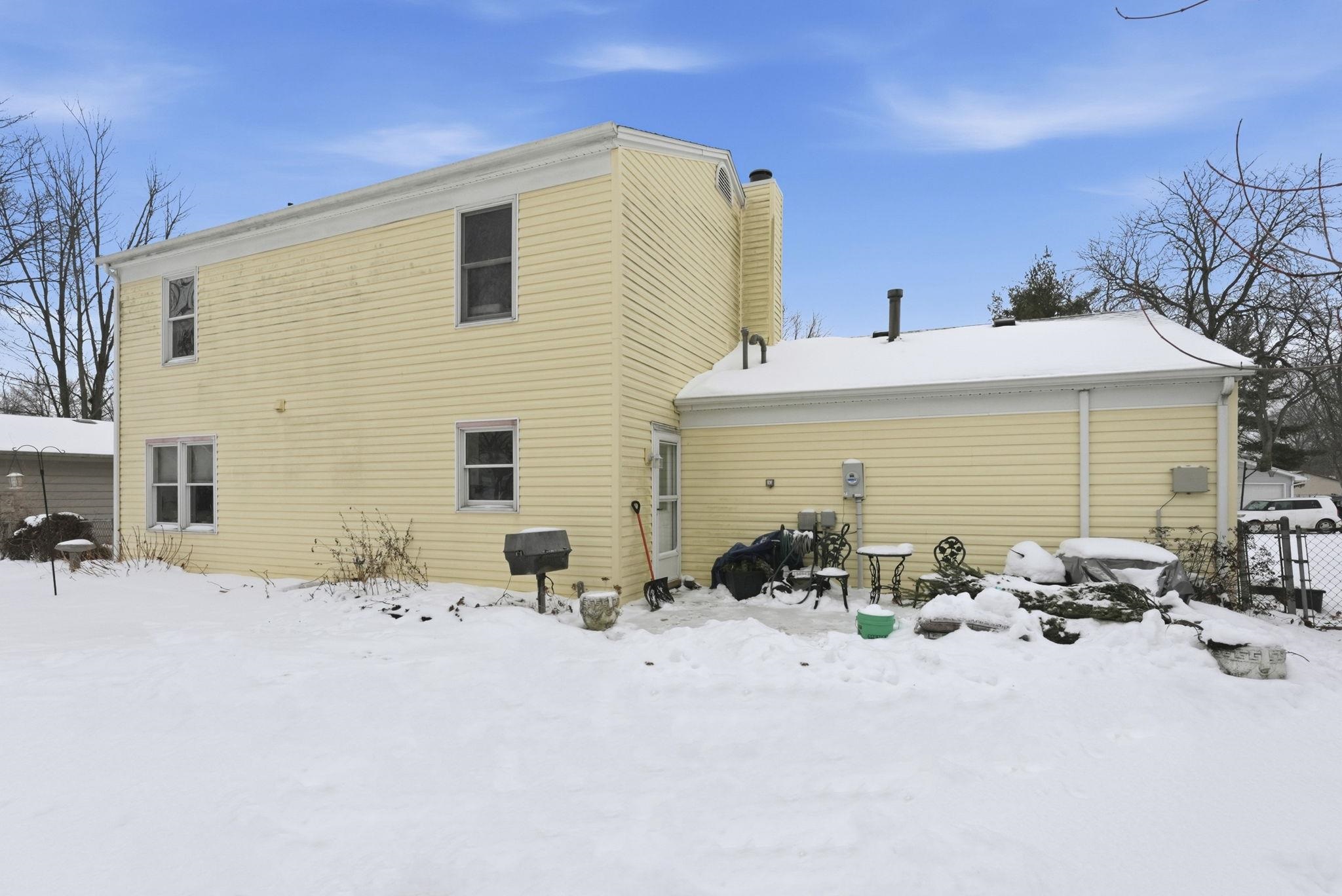 Snow covered rear of property featuring a patio and a chimney