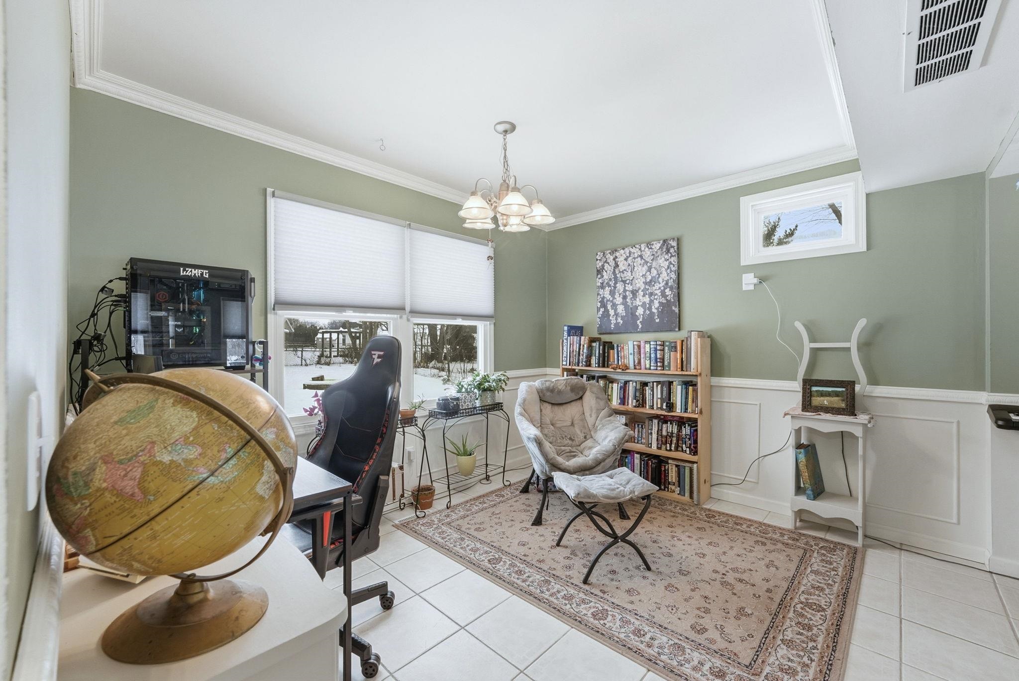 Home office featuring suspended lighting, crown molding, wainscoting, light tile patterned floors, and a decorative wall