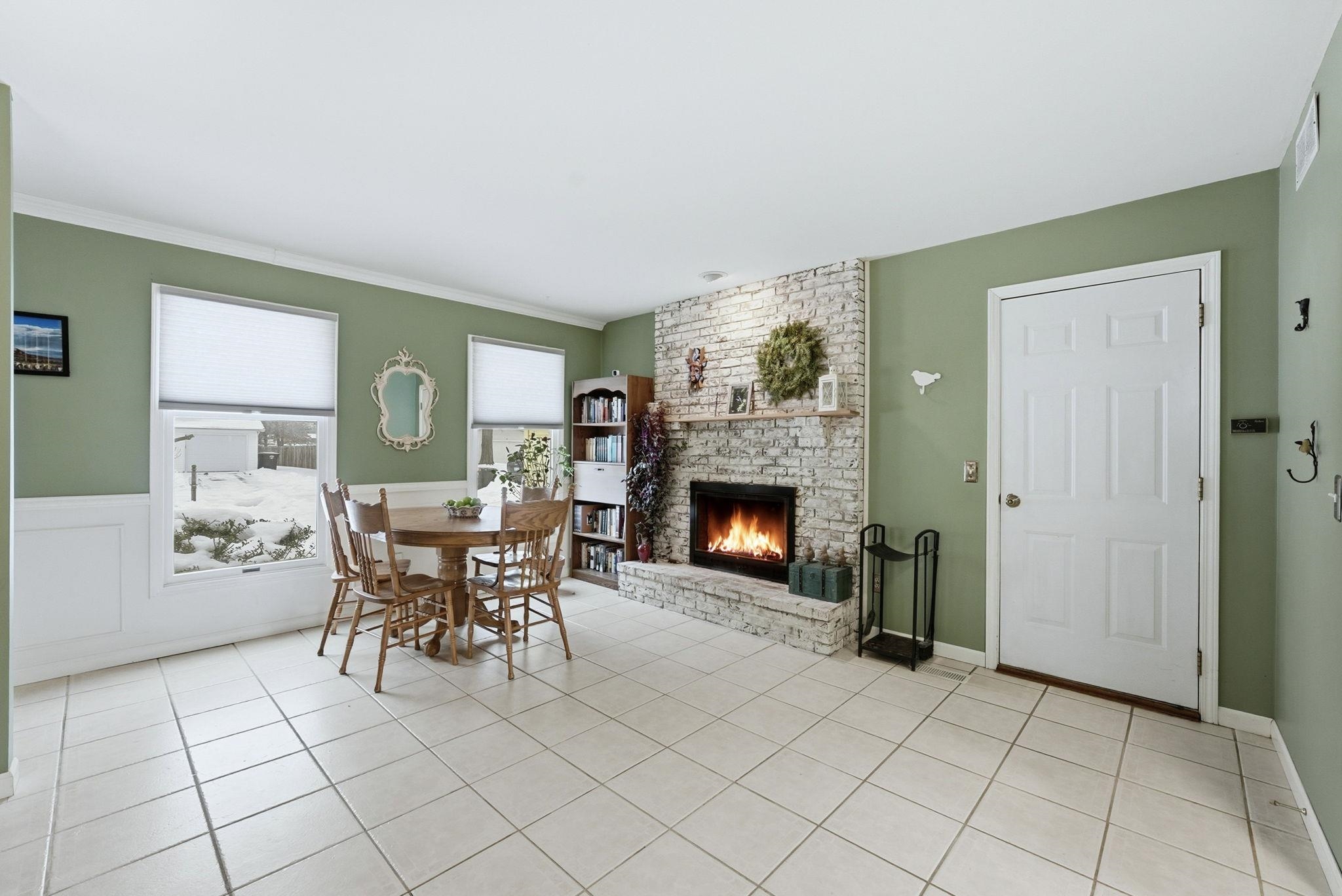 Dining space featuring a fireplace, light tile patterned floors, and a wainscoted wall