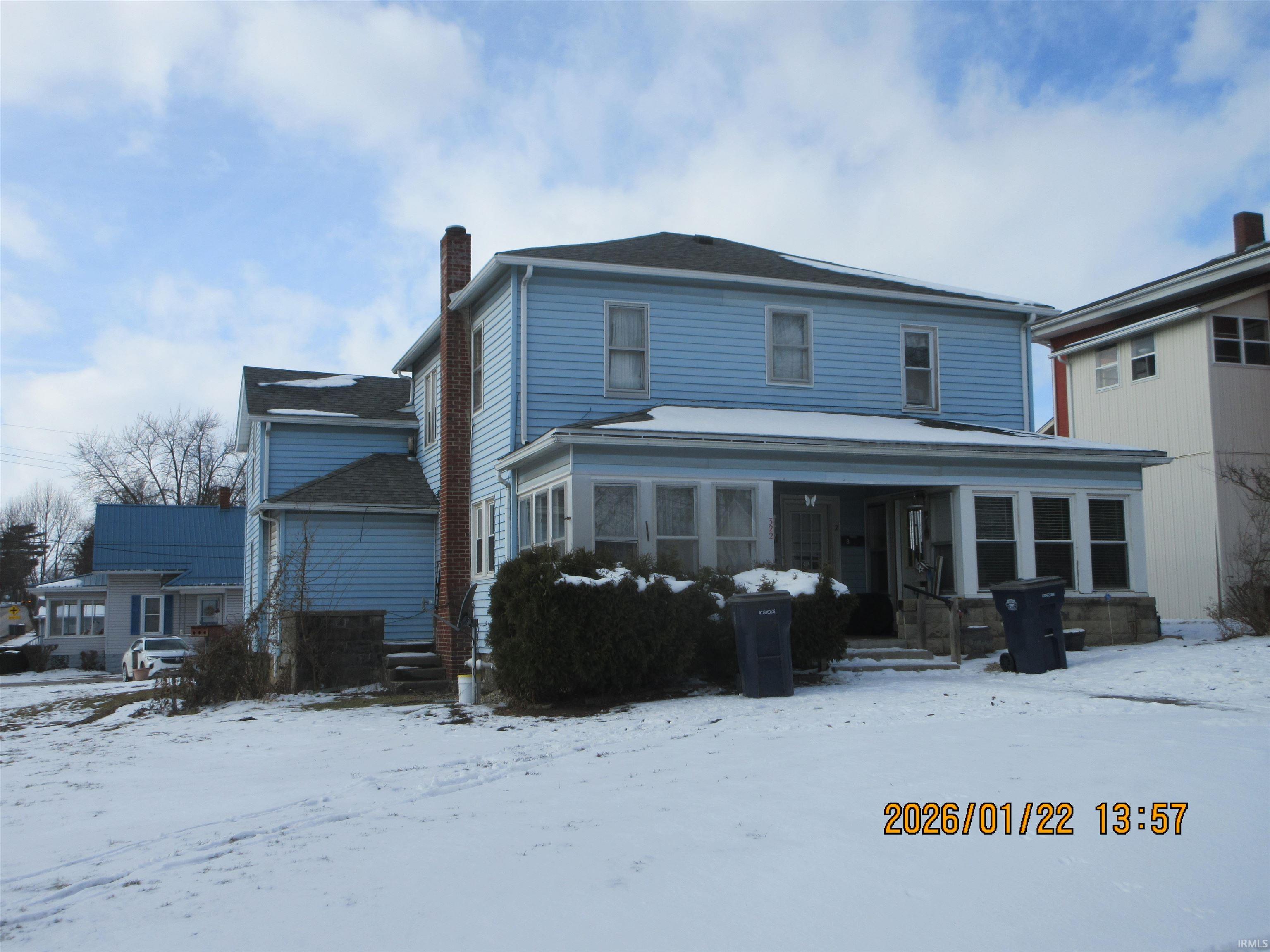 Snow covered rear of property featuring a sunroom and a chimney