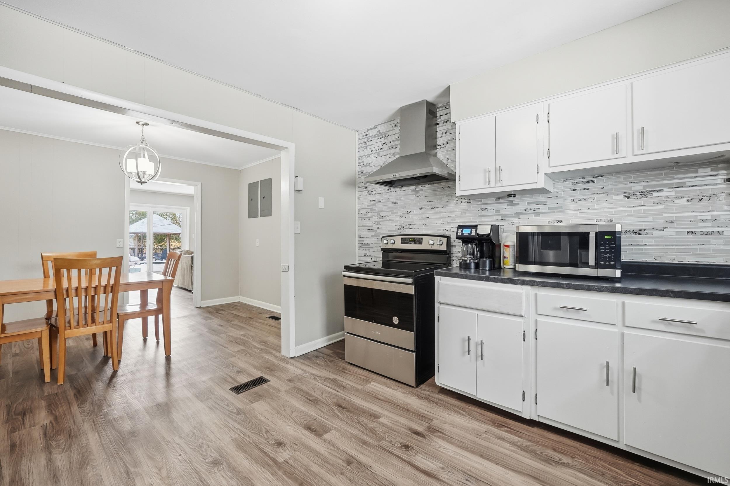 Kitchen with stainless steel appliances, dark countertops, white cabinets, light wood-style floors, and tasteful backsplash
